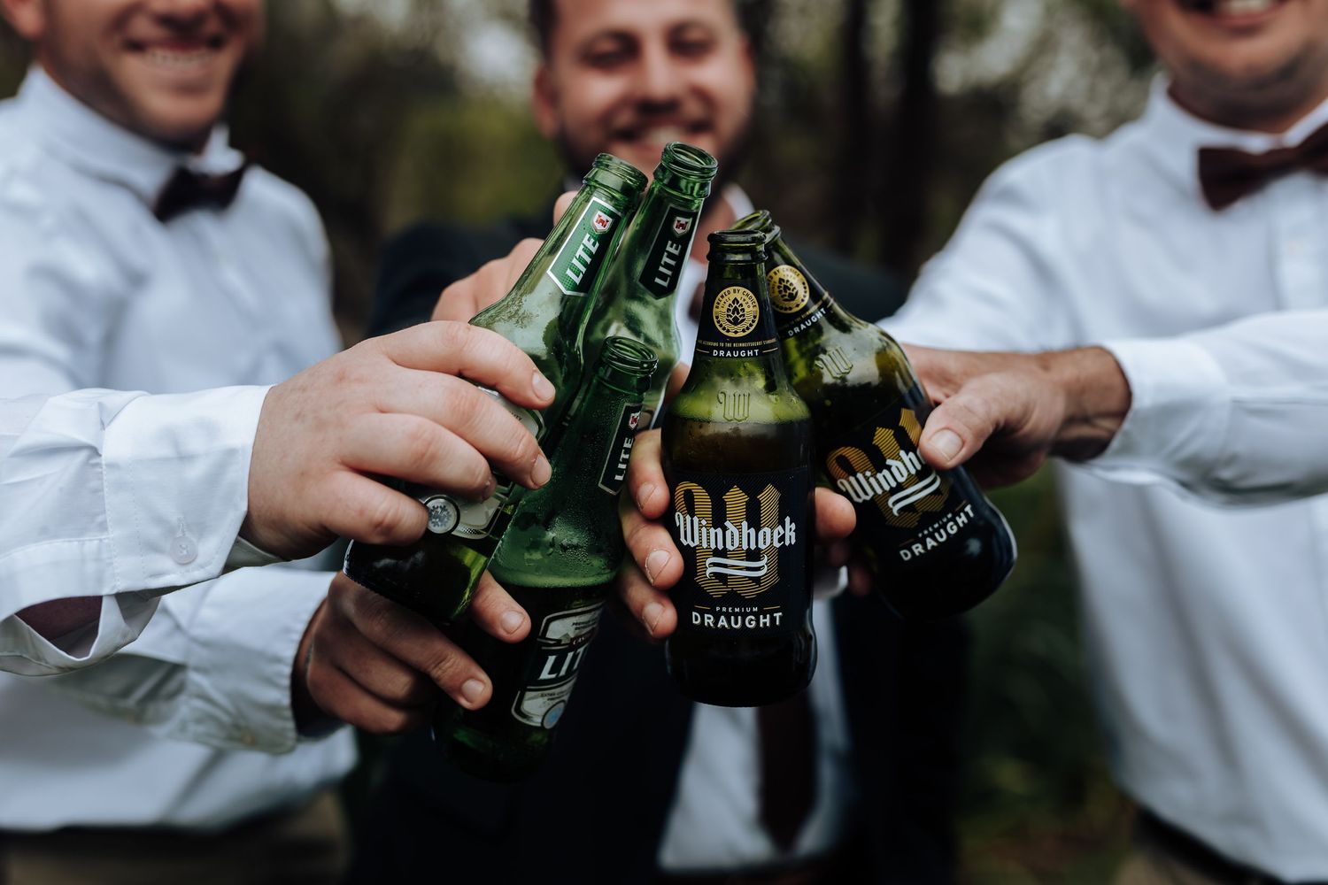 People in formal attire holding and clinking beer bottles together in celebration.