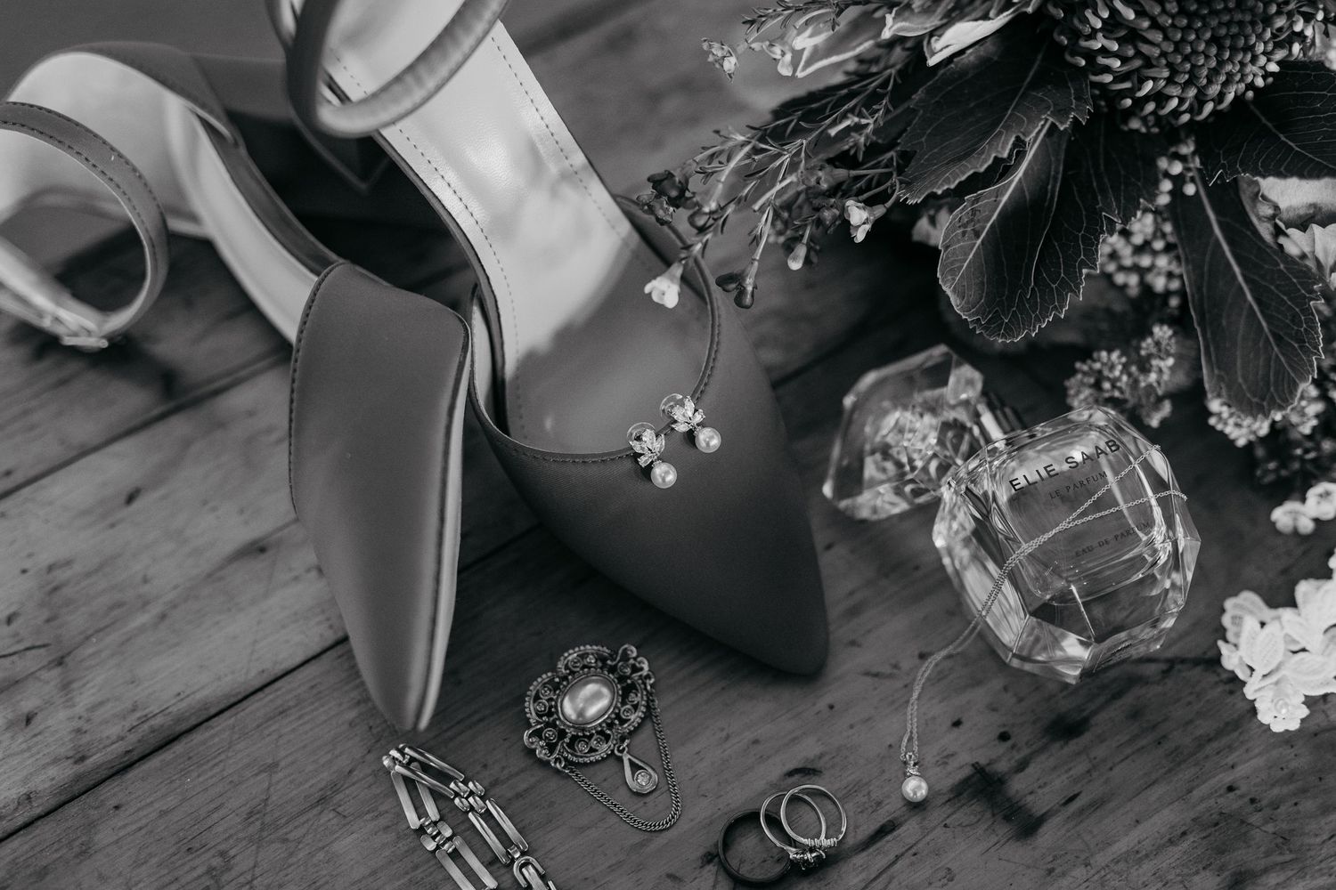 Black and white wedding details including rings, flowers, and accessories arranged on a rustic wooden surface.