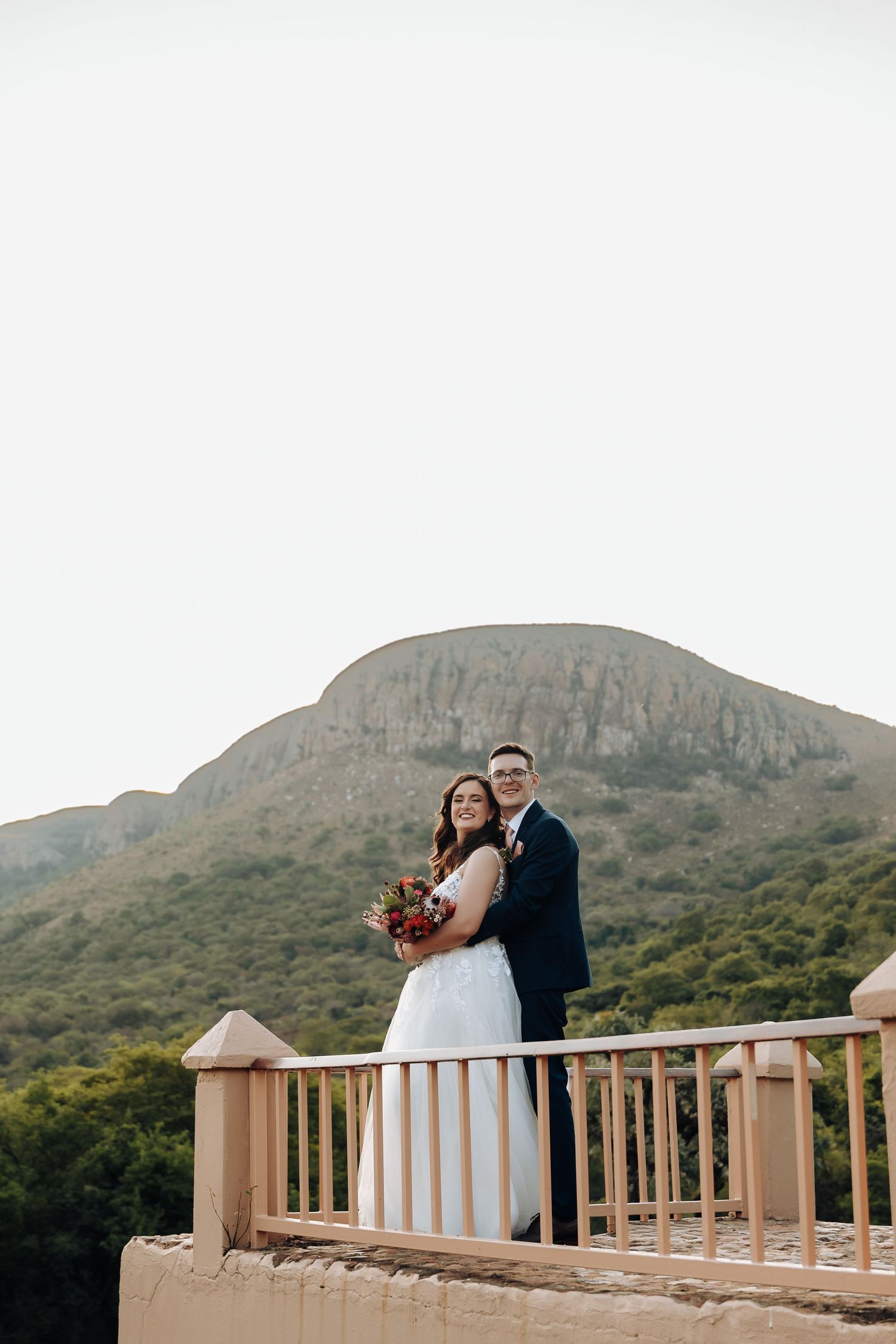 A couple shares romantic moments on a scenic mountain overlook with wooden railings during their wedding photoshoot.