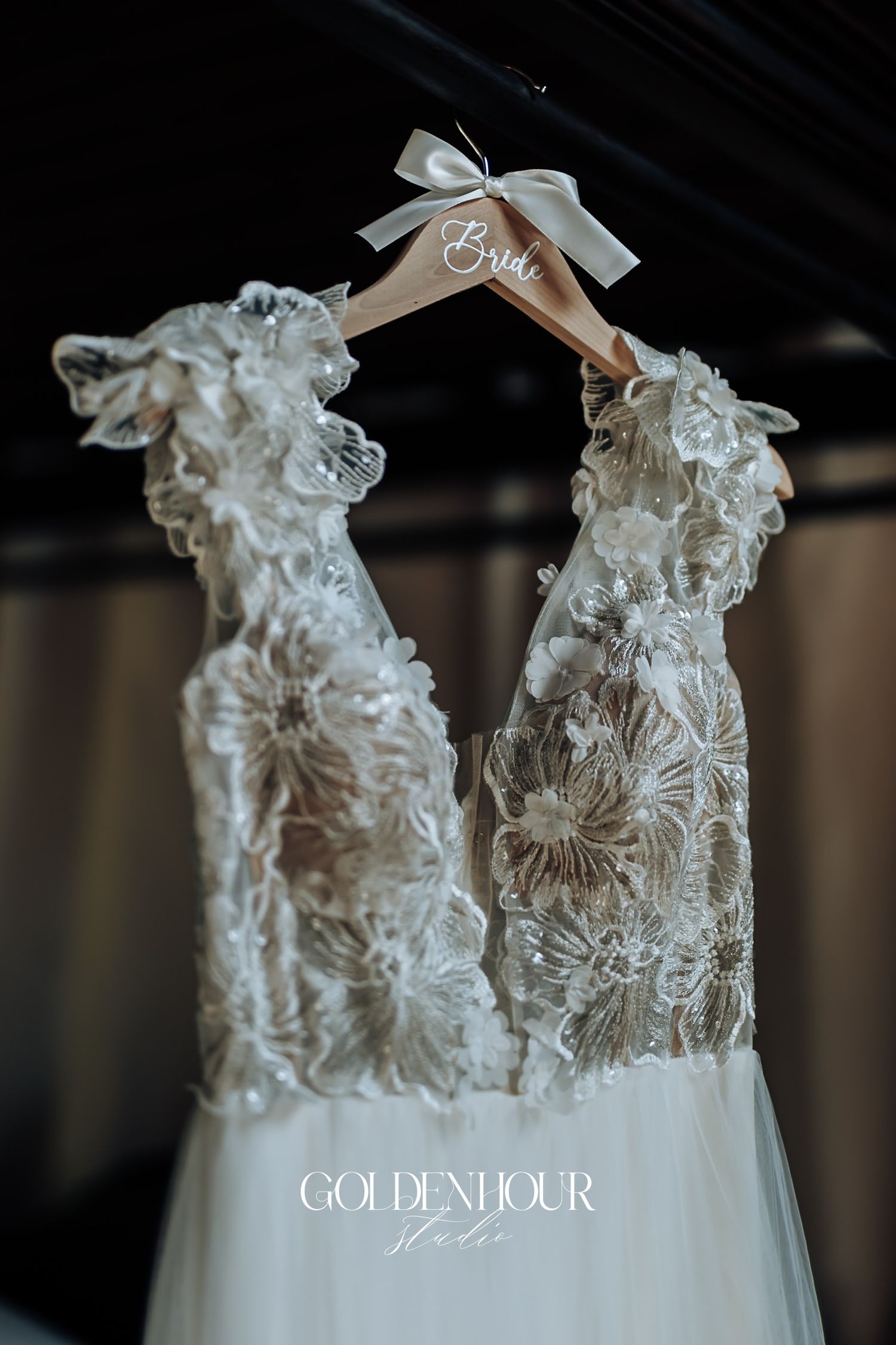 Elegant lace wedding dress with floral appliques hanging on a wooden Bride hanger.
