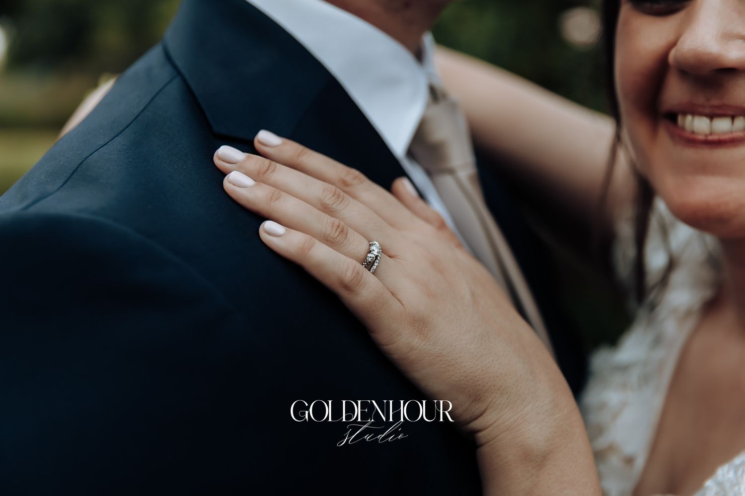 Close-up of bride's hand with diamond engagement ring resting on groom's navy suit jacket.