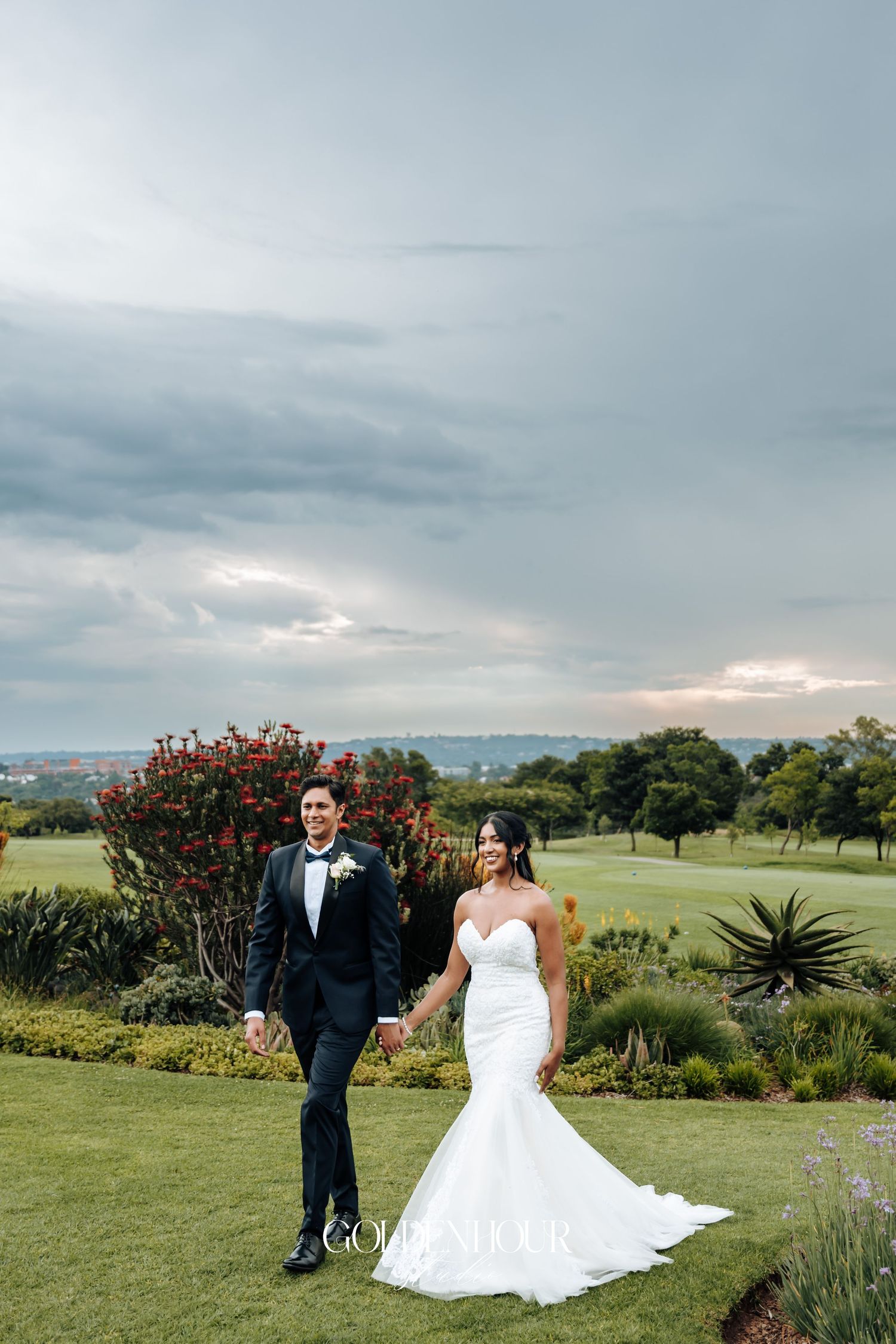 Wedding couple posing in a lush garden landscape with cloudy sky backdrop.