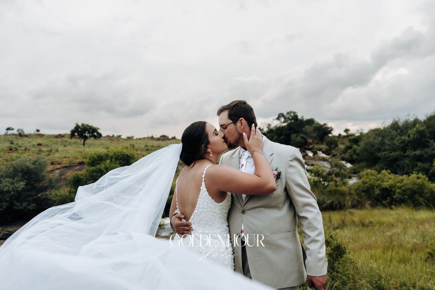 Romantic wedding couple embraces in an outdoor field setting with cloudy skies in the background.