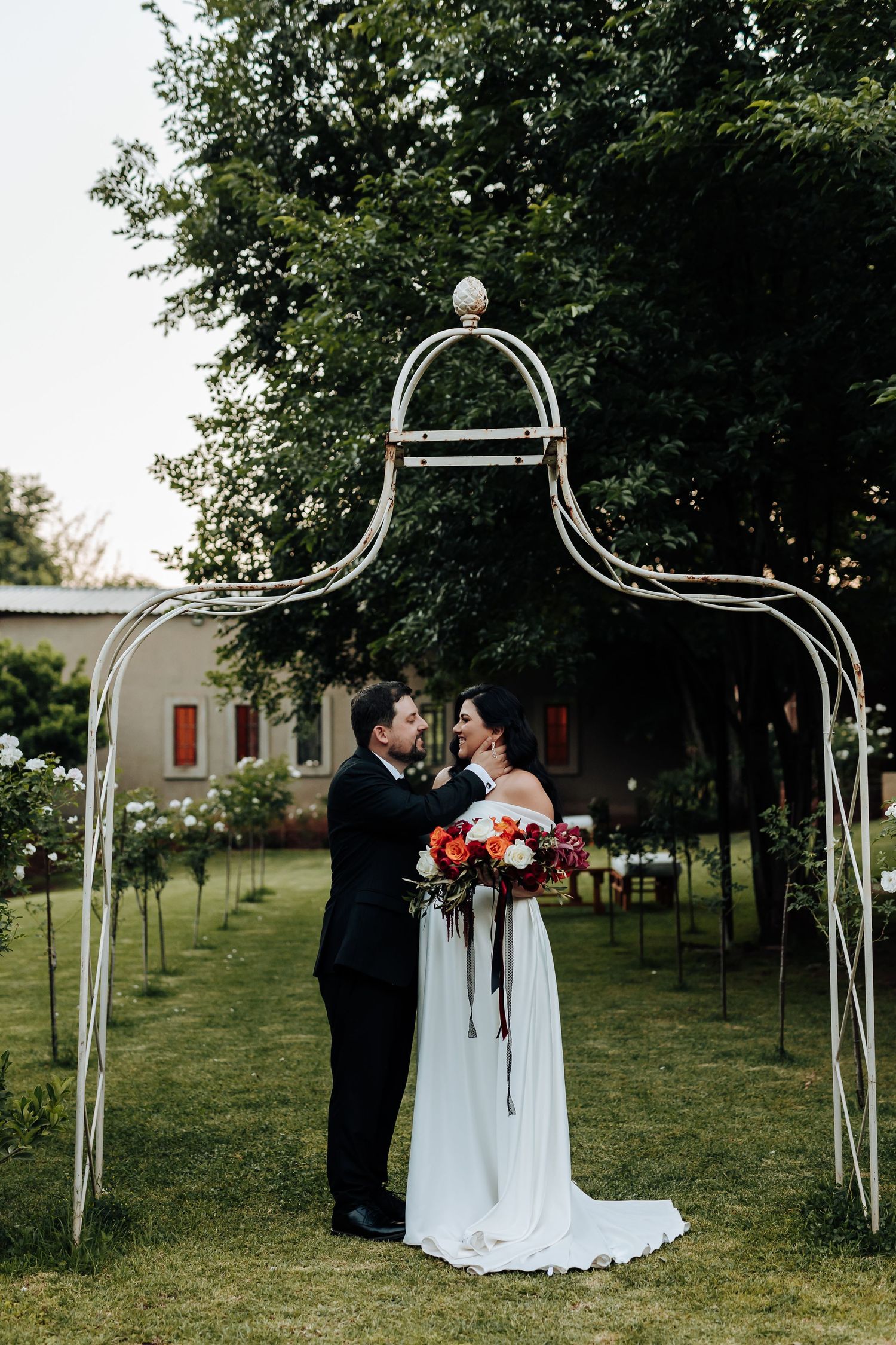 Wedding ceremony setup with white metal arches in a garden setting.