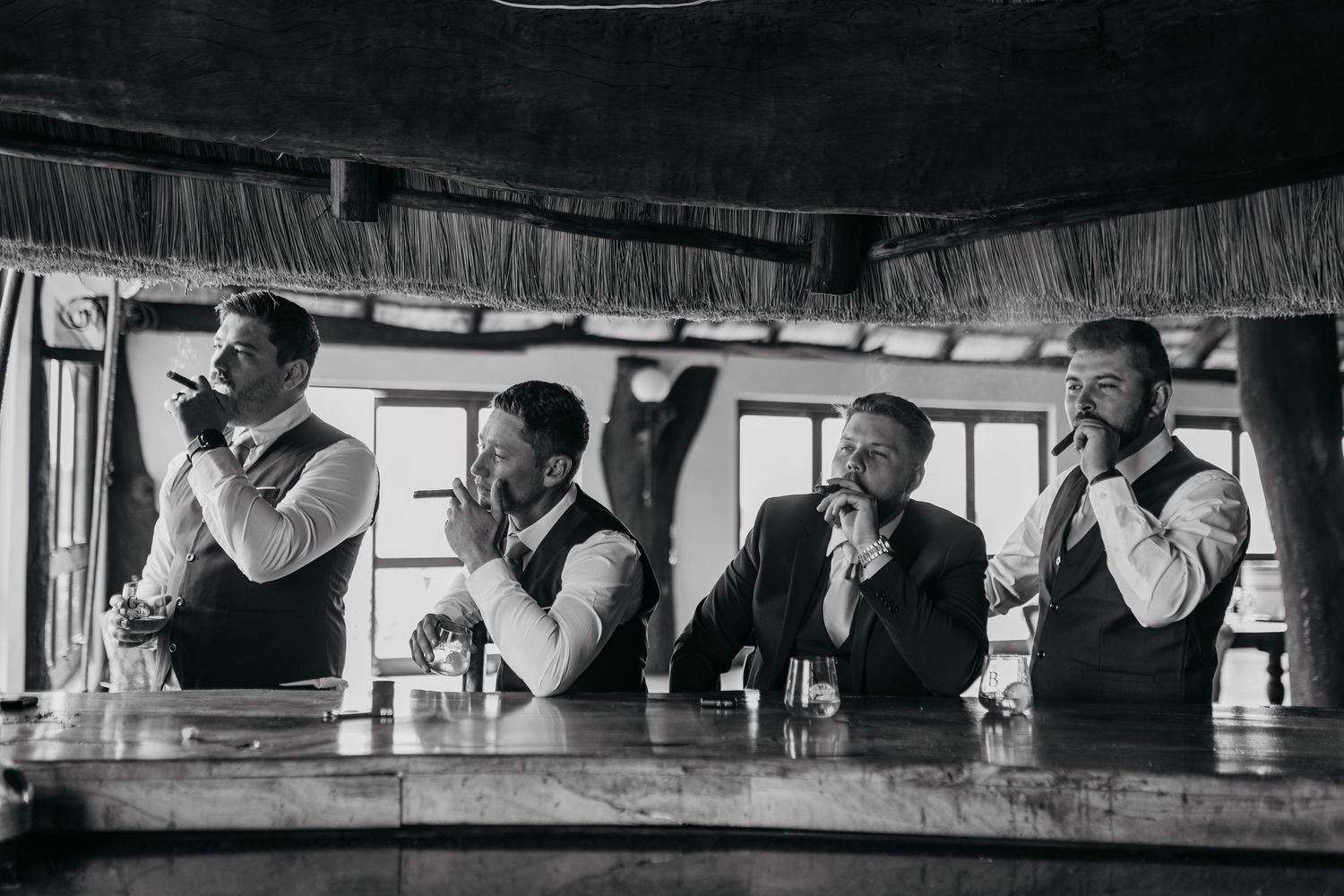 Vintage black and white photograph of four men in formal attire drinking at a bar counter.
