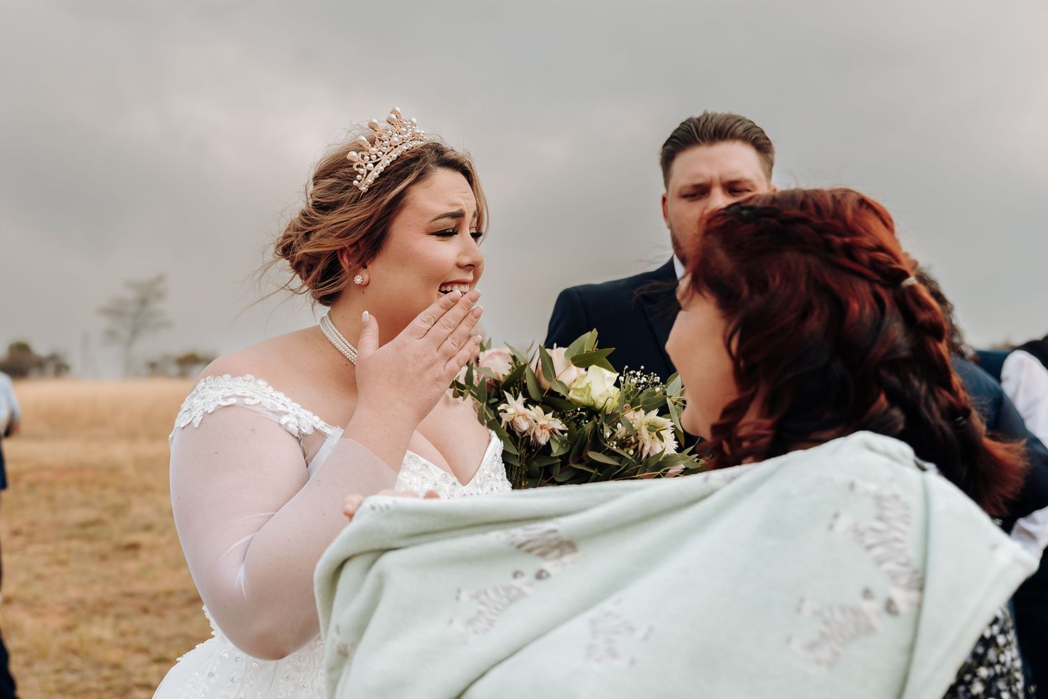 A joyful wedding moment captured outdoors with white flowers and winter field backdrop.