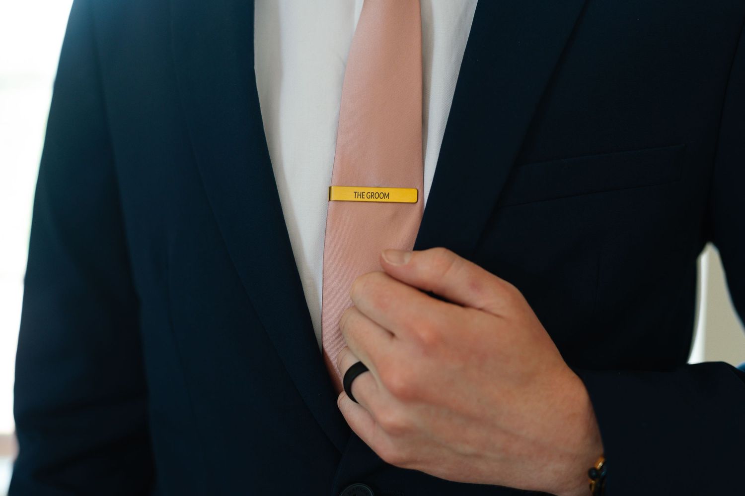 Professional in a black suit and white shirt adjusts their tie while standing against a dark background.