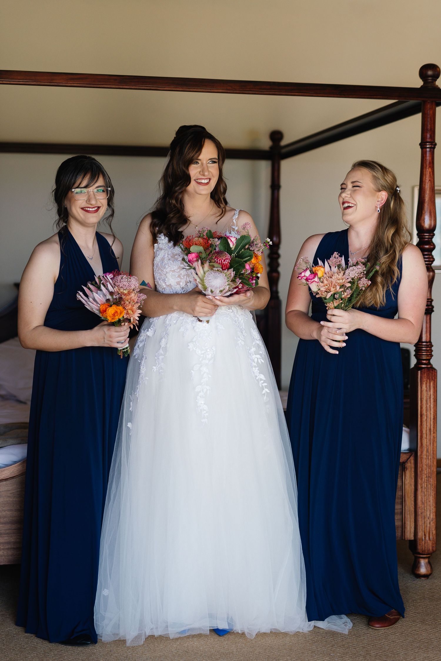 Wedding party members in navy blue dresses gather around bride in white gown during celebration.