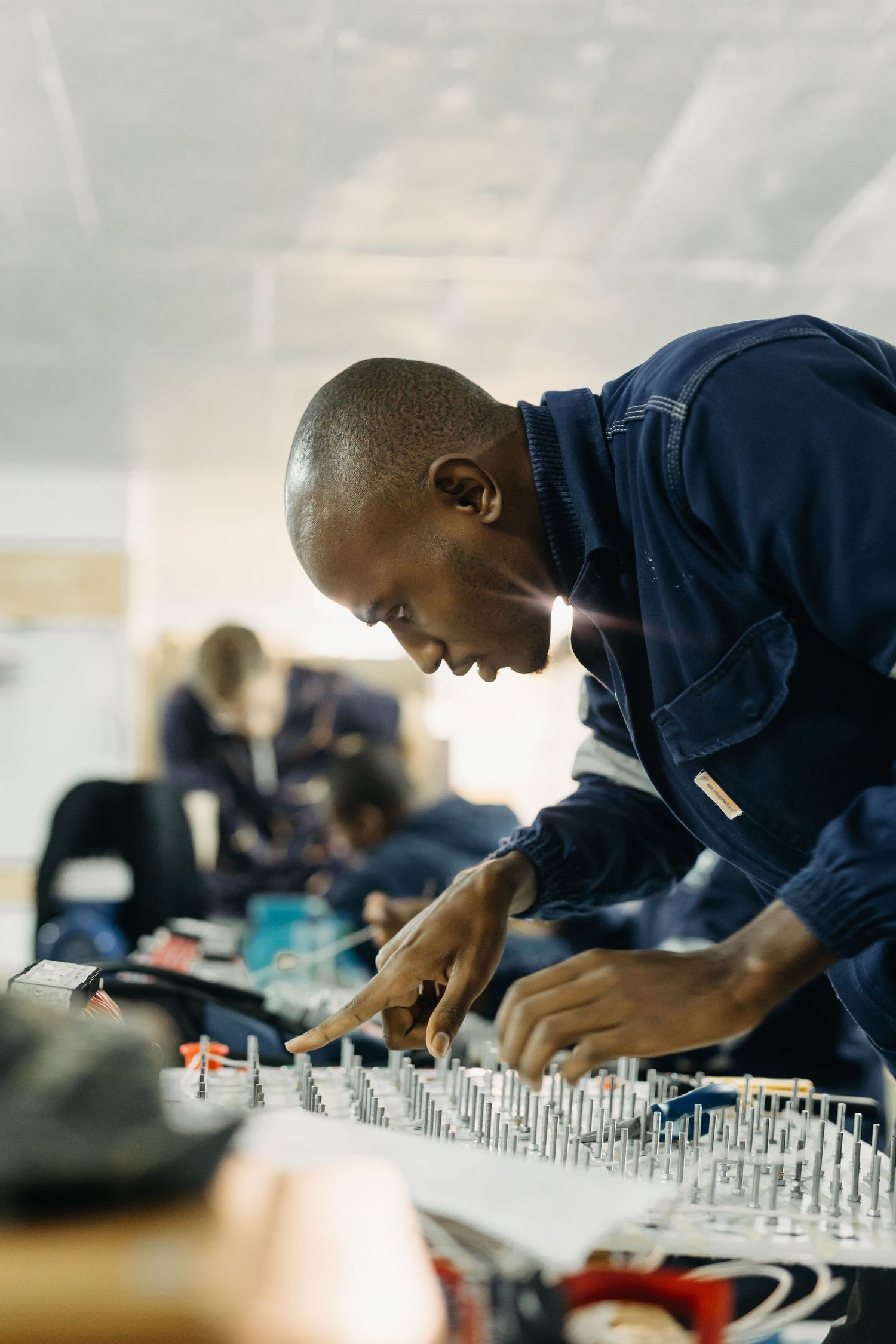 Person in navy blue jacket working intently at a sound mixing board with audio equipment in studio setting.