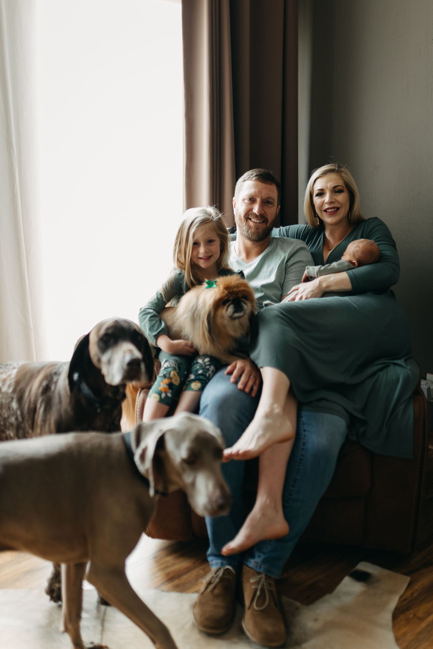Family relaxes together on couch with their beloved pets including dogs and guinea pig in cozy living room setting.