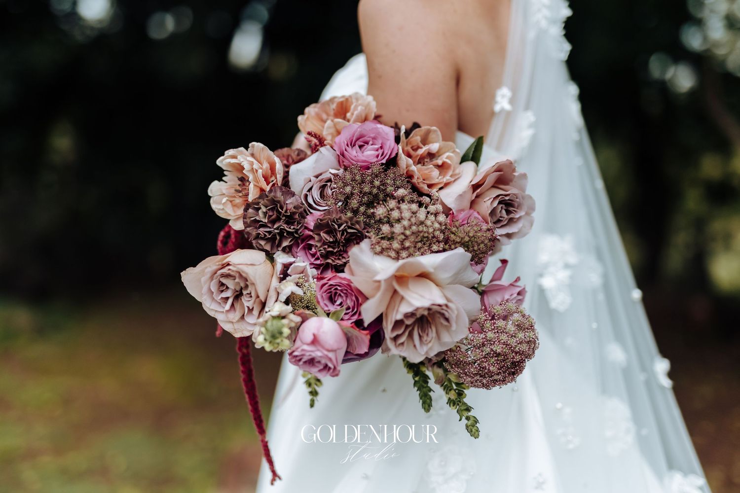 Close-up of a lush bridal bouquet with pink roses, dahlias, and berries against a white lace gown.