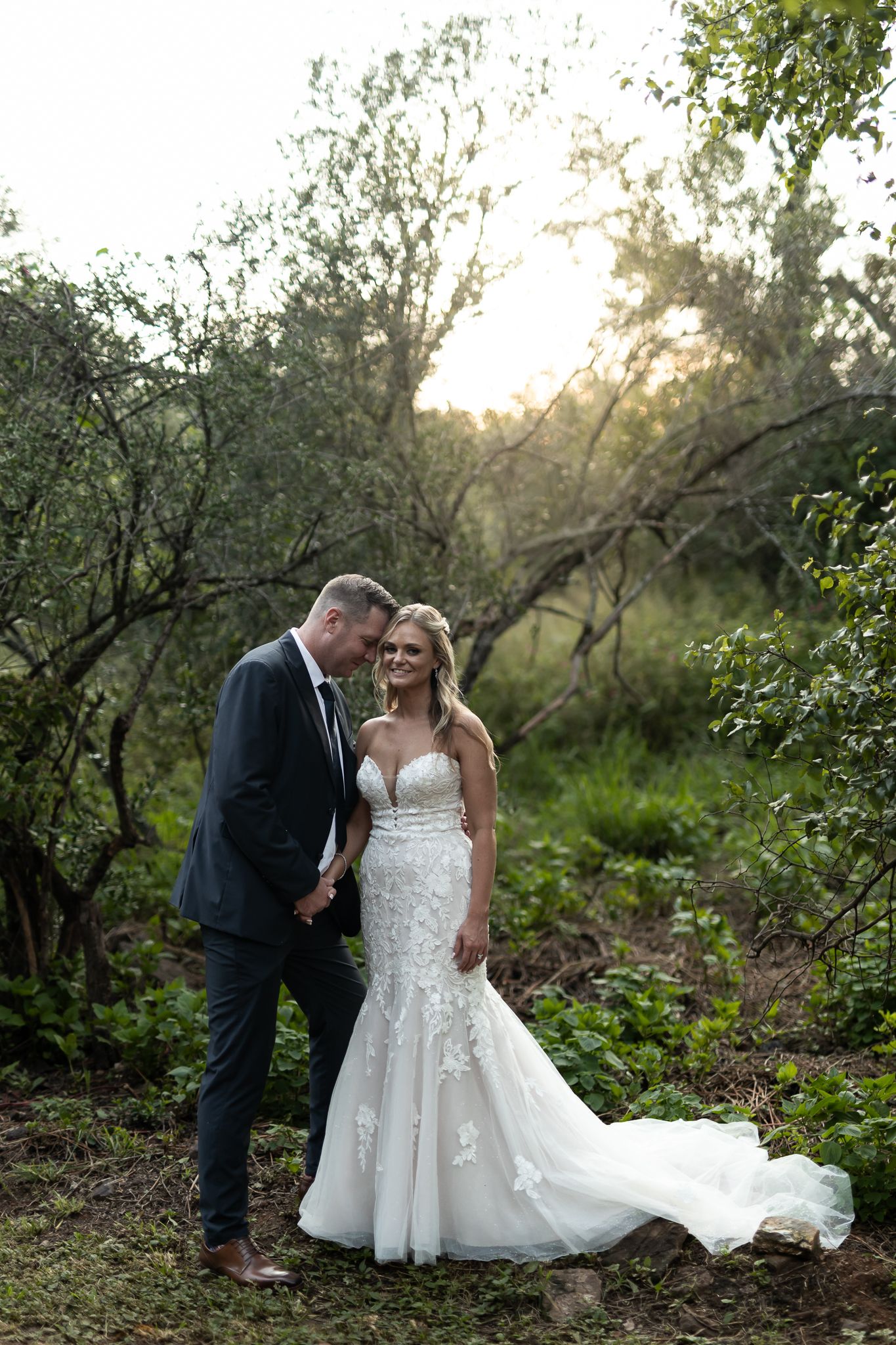 A romantic wedding portrait captured in a natural wooded setting during golden hour.