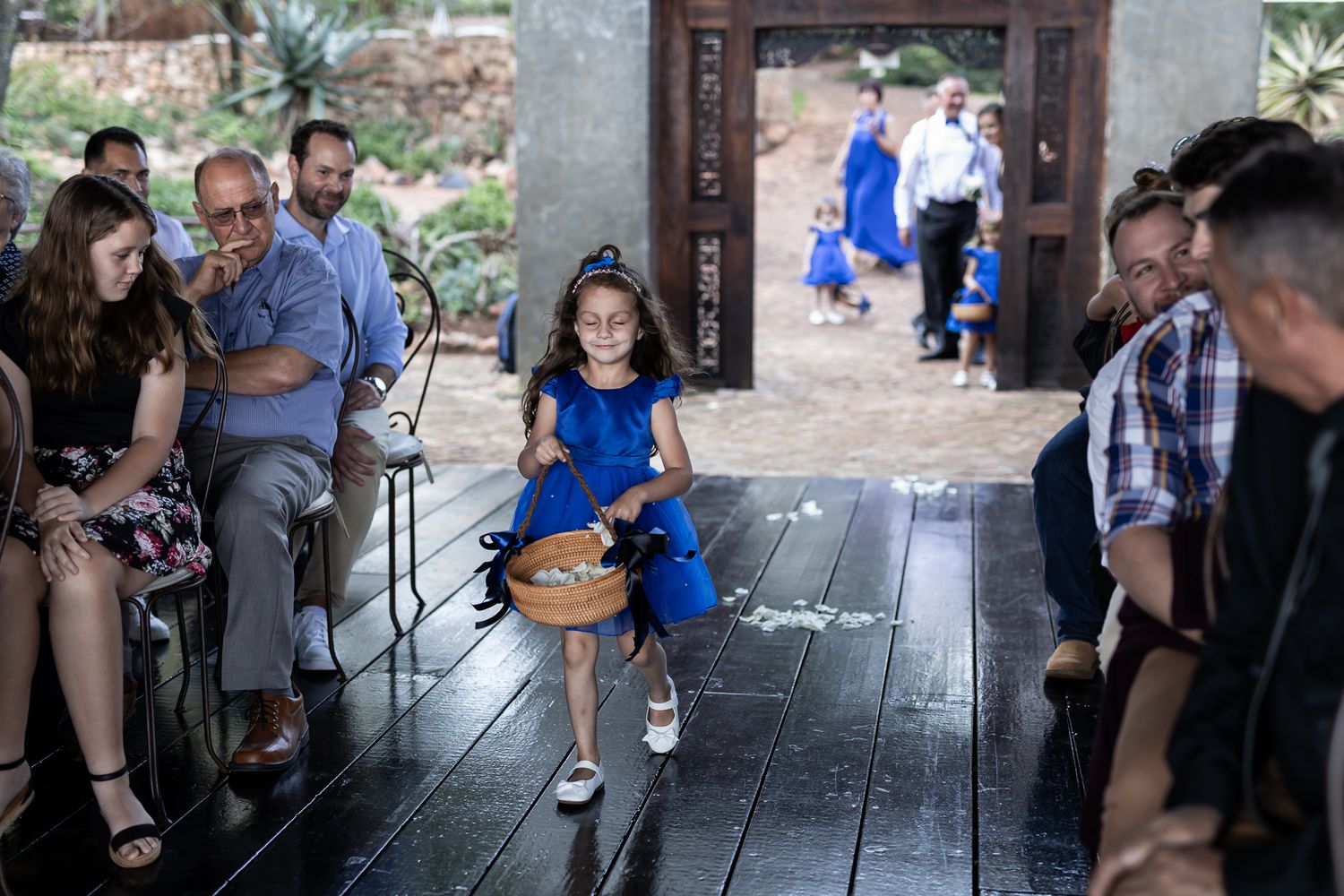 Young flower girl in bright blue dress walks down wooden aisle during wedding ceremony.