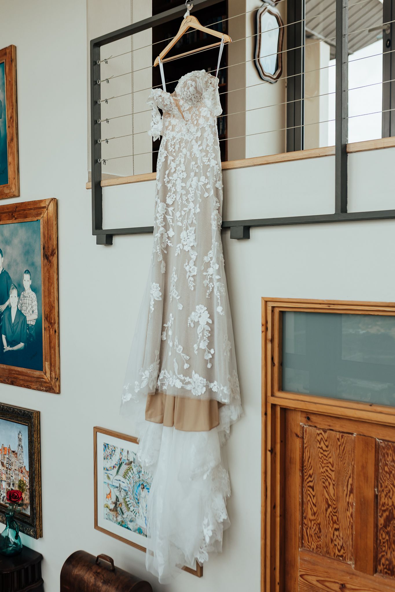 Lace wedding dress with delicate details hanging on display among framed artwork.