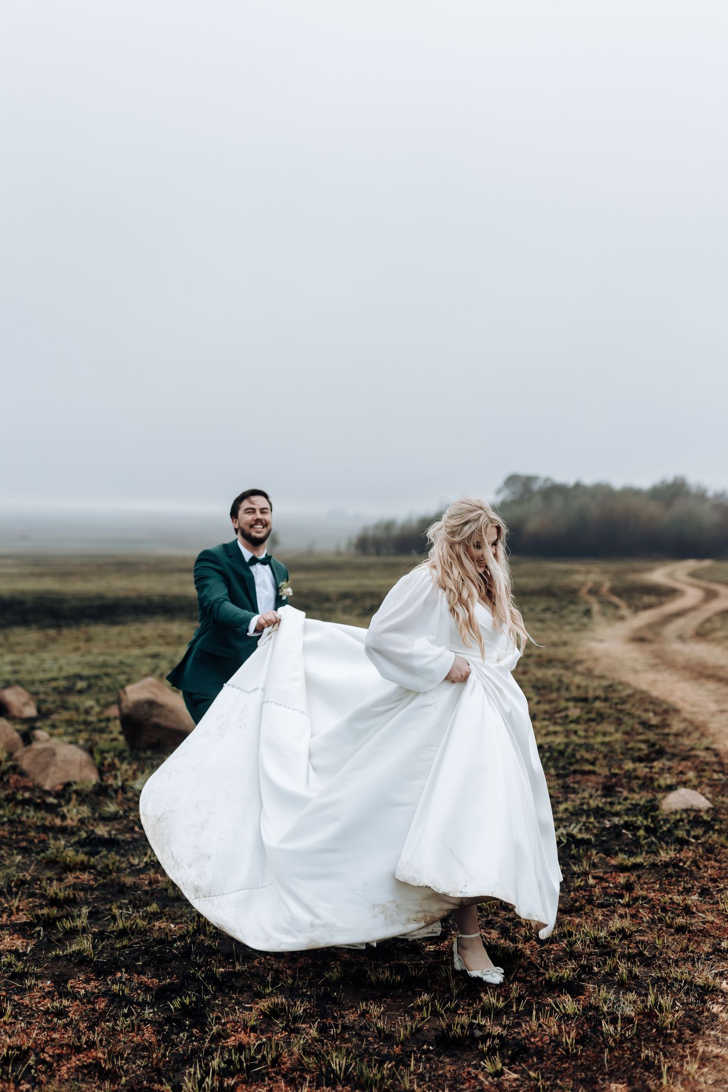 Newlyweds dance together on a rustic dirt path surrounded by open fields.