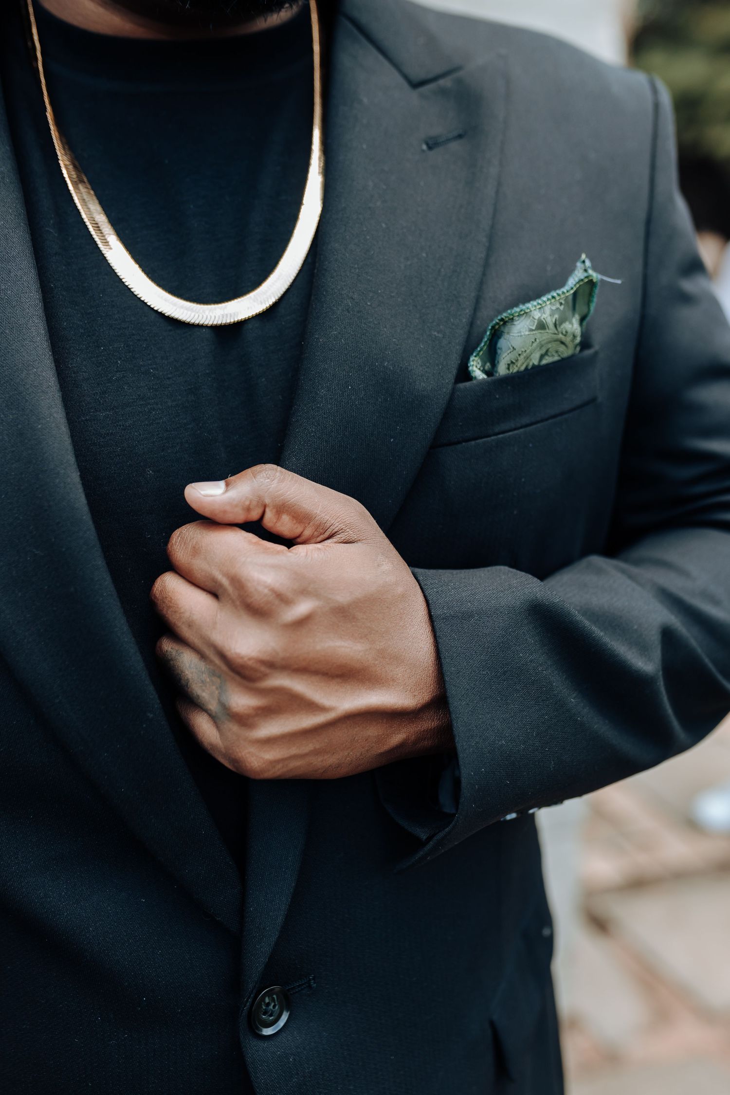 Close-up of dark suit jacket with patterned pocket square and silver chain necklace.