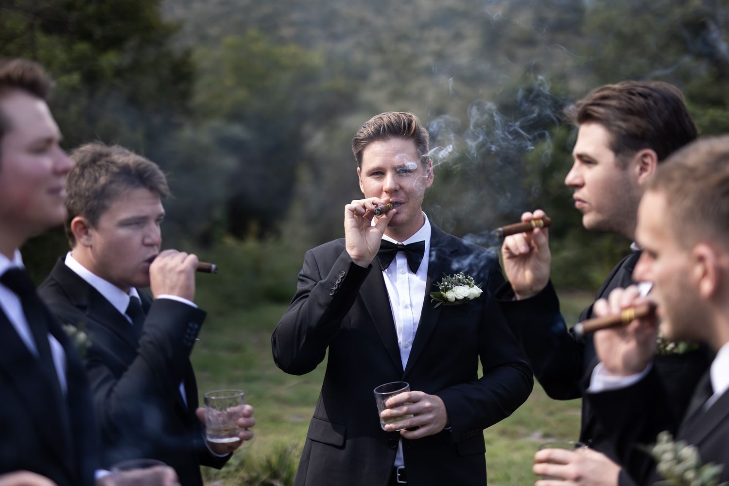 Groomsmen enjoying cigars during an outdoor wedding celebration.