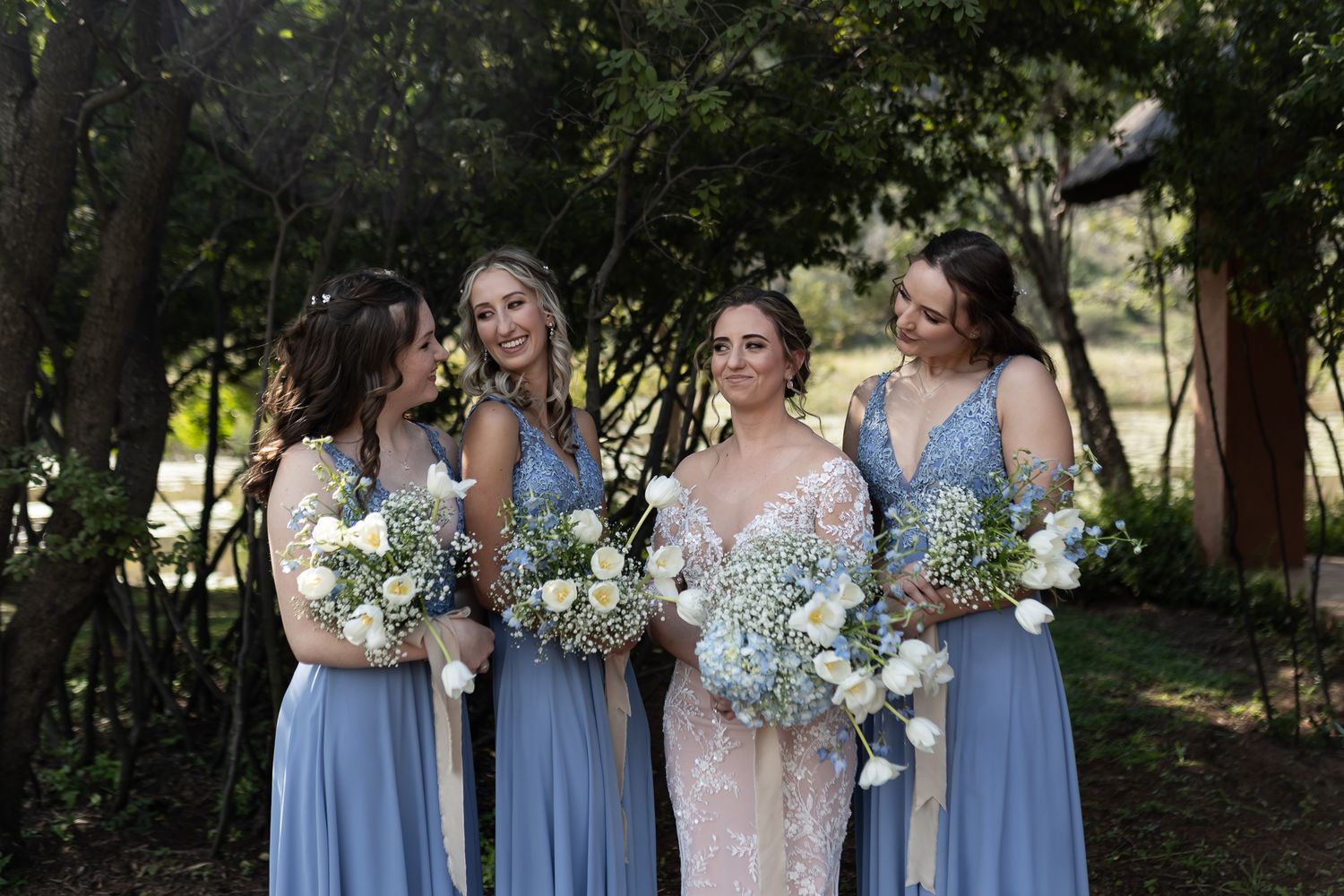 A bridal party in blue dresses holding matching bouquets of white flowers and baby's breath.