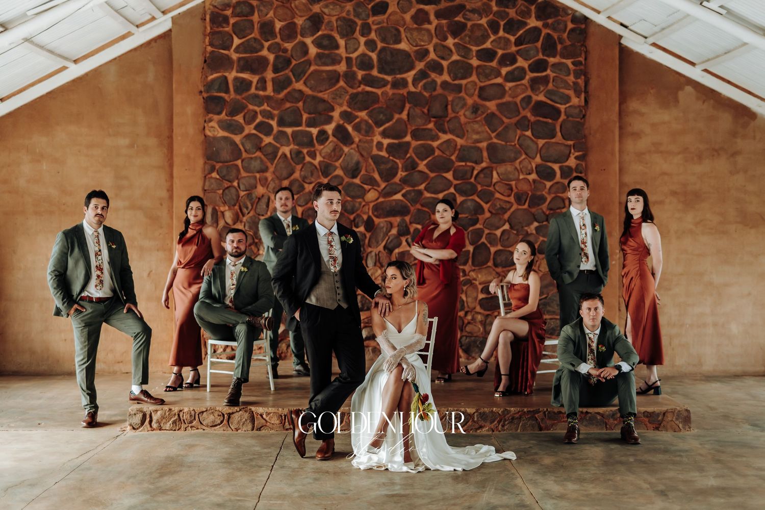 Wedding party and guests pose for a panoramic group photo against a textured stone wall.