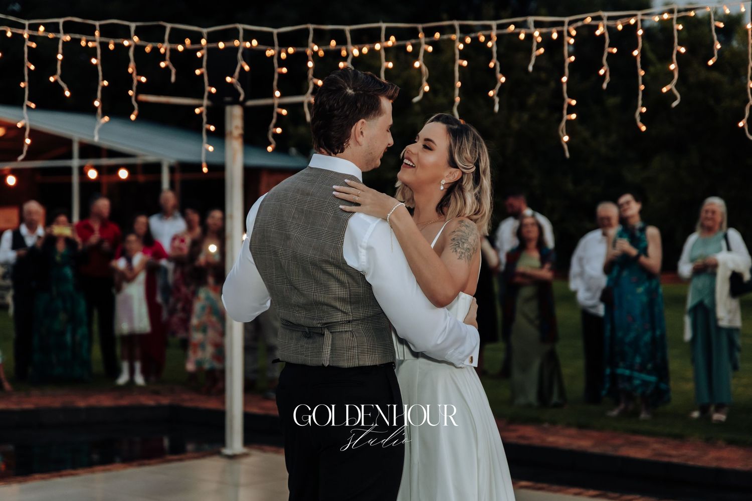 Evening wedding reception under string lights with dancing couples.