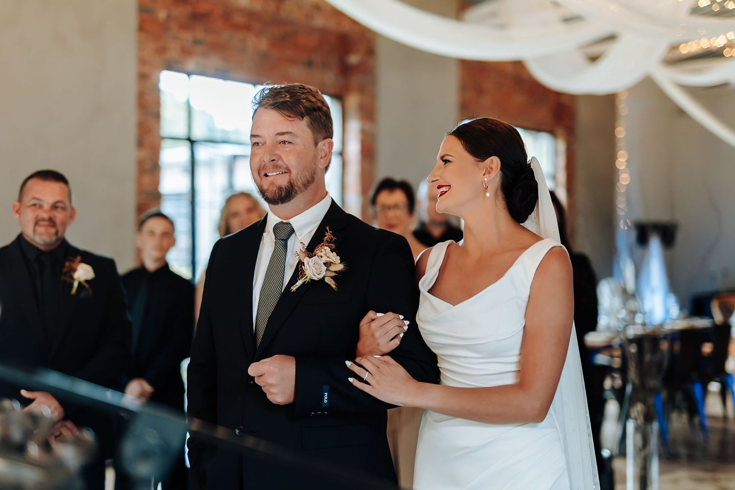 Emotional wedding ceremony moment captured in an elegant indoor venue with white draping and crystal chandeliers.