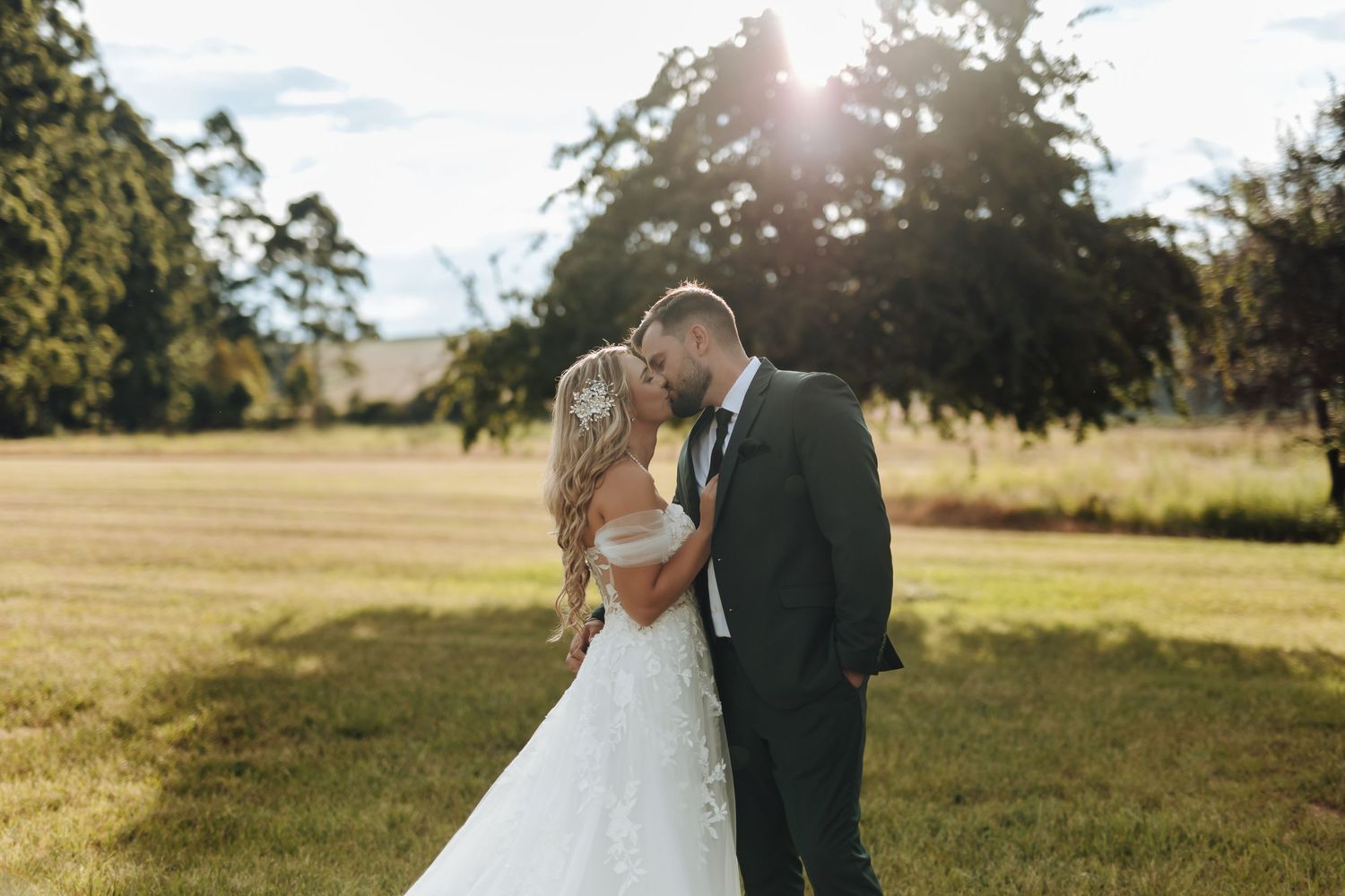 A couple shares a romantic moment in a sunlit field during their wedding ceremony.