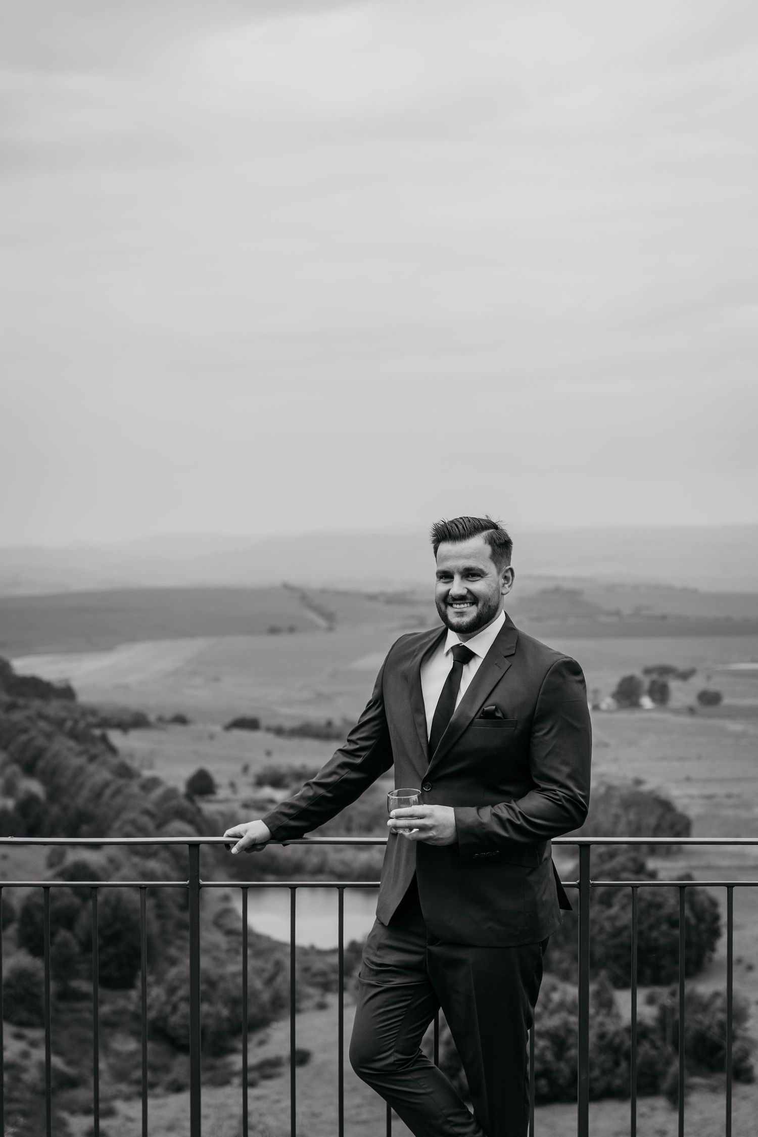Black and white panoramic series showing a person in a suit standing by a railing overlooking a scenic valley landscape.