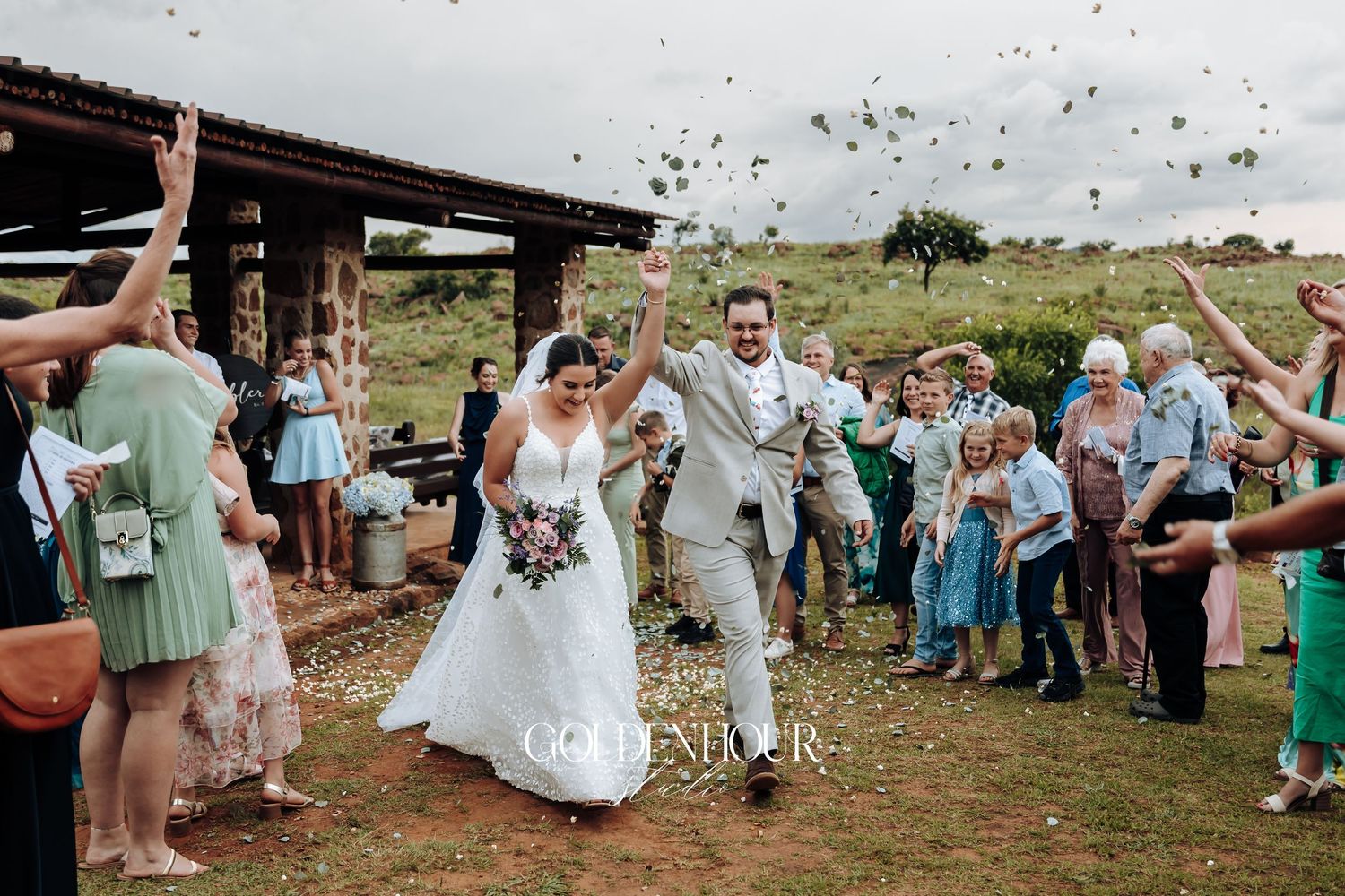 Wedding guests toss confetti in celebration during an outdoor ceremony.
