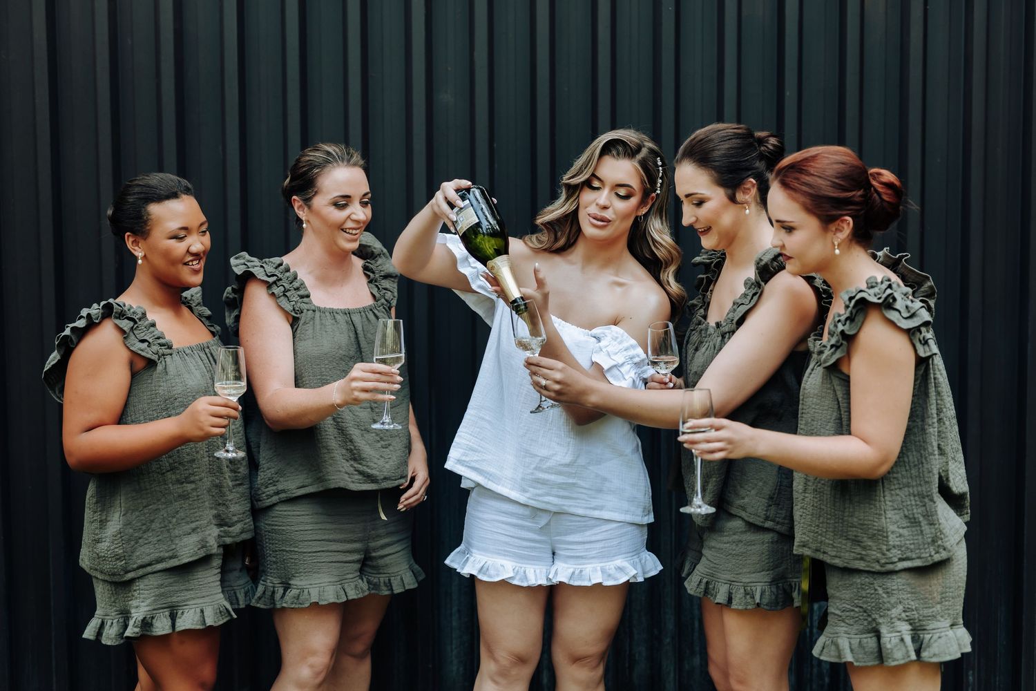 Friends in olive green and white dresses laughing together during a celebration.