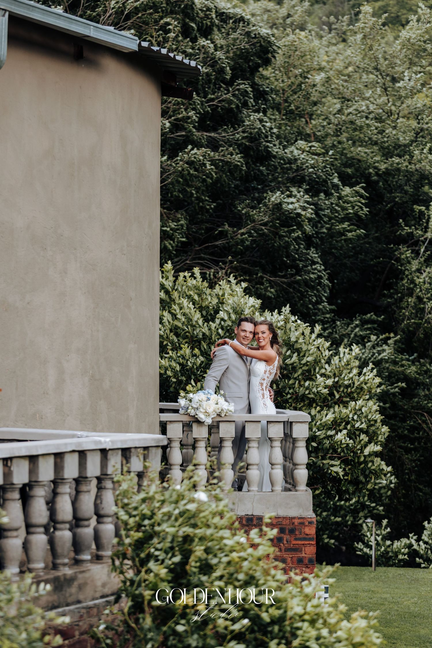 Romantic wedding couple shares intimate moments along an elegant stone balustrade in a lush garden setting.