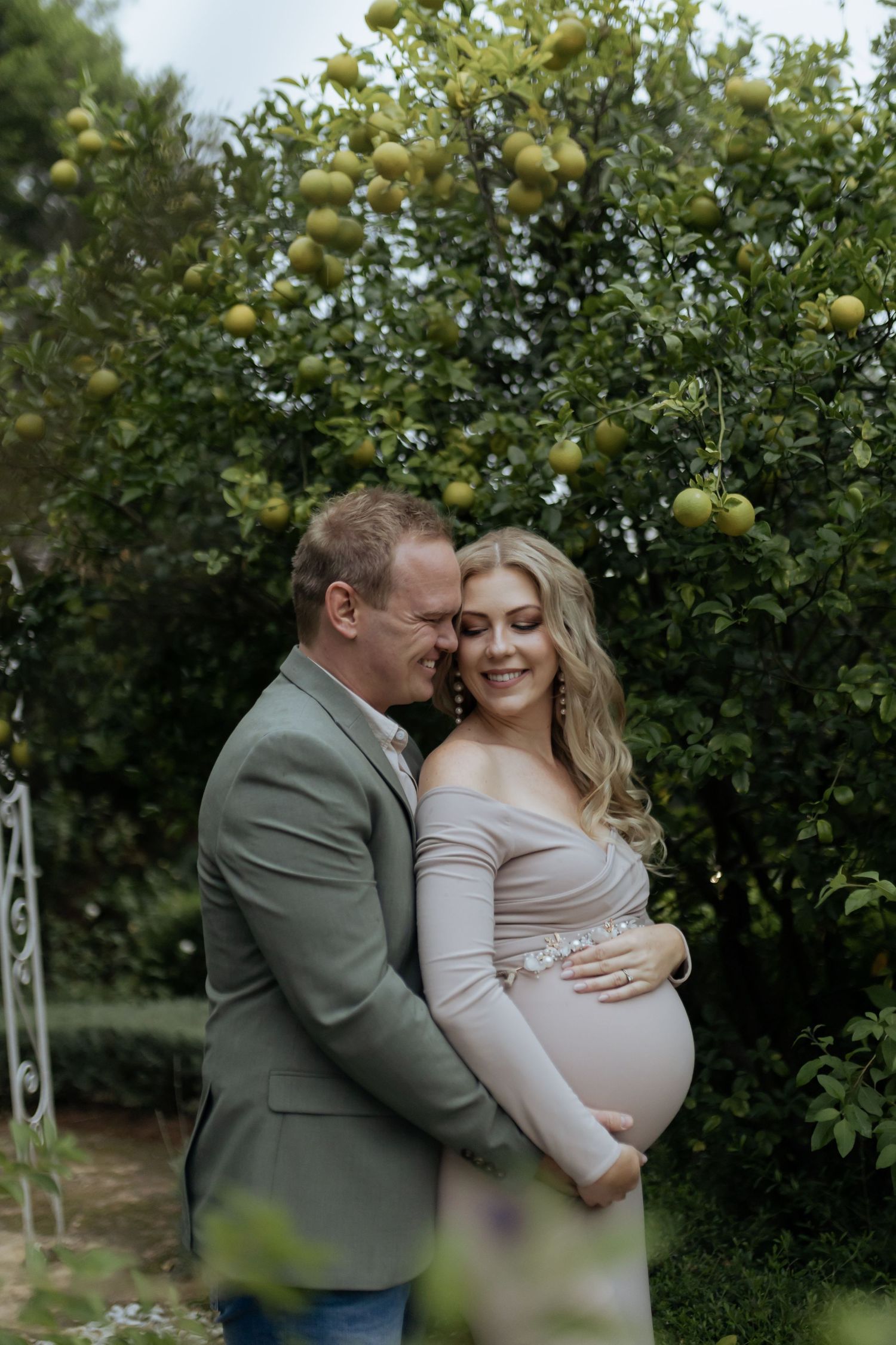 An intimate maternity session among blooming citrus trees in a garden.