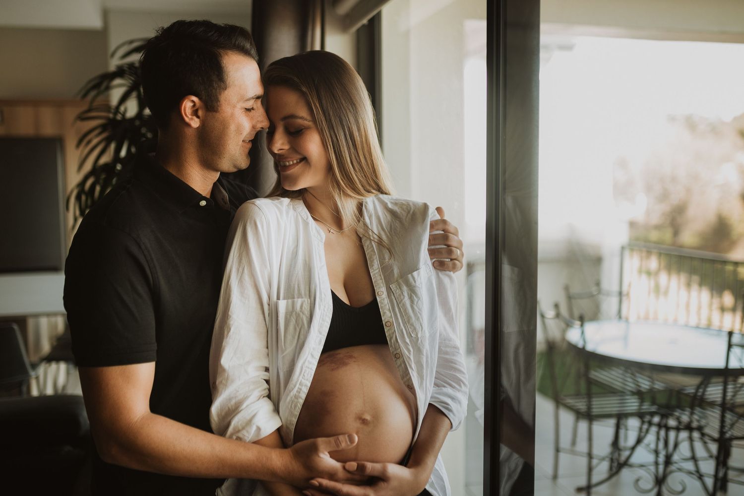 Romantic lifestyle photos capture couple's tender moments by window in bright interior setting.