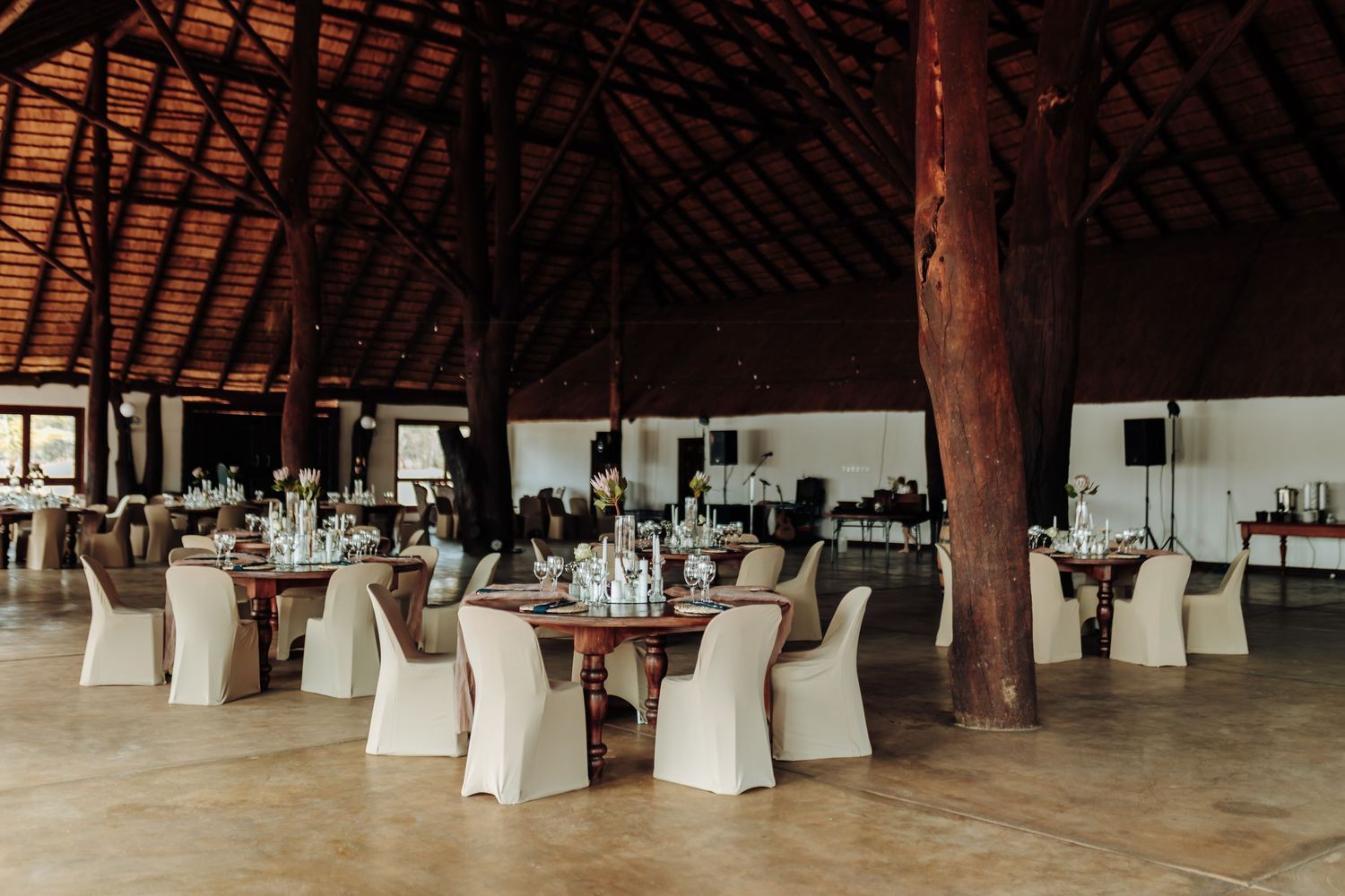 An elegant banquet hall with wooden beams, round tables and white chair covers set for a formal dining event.