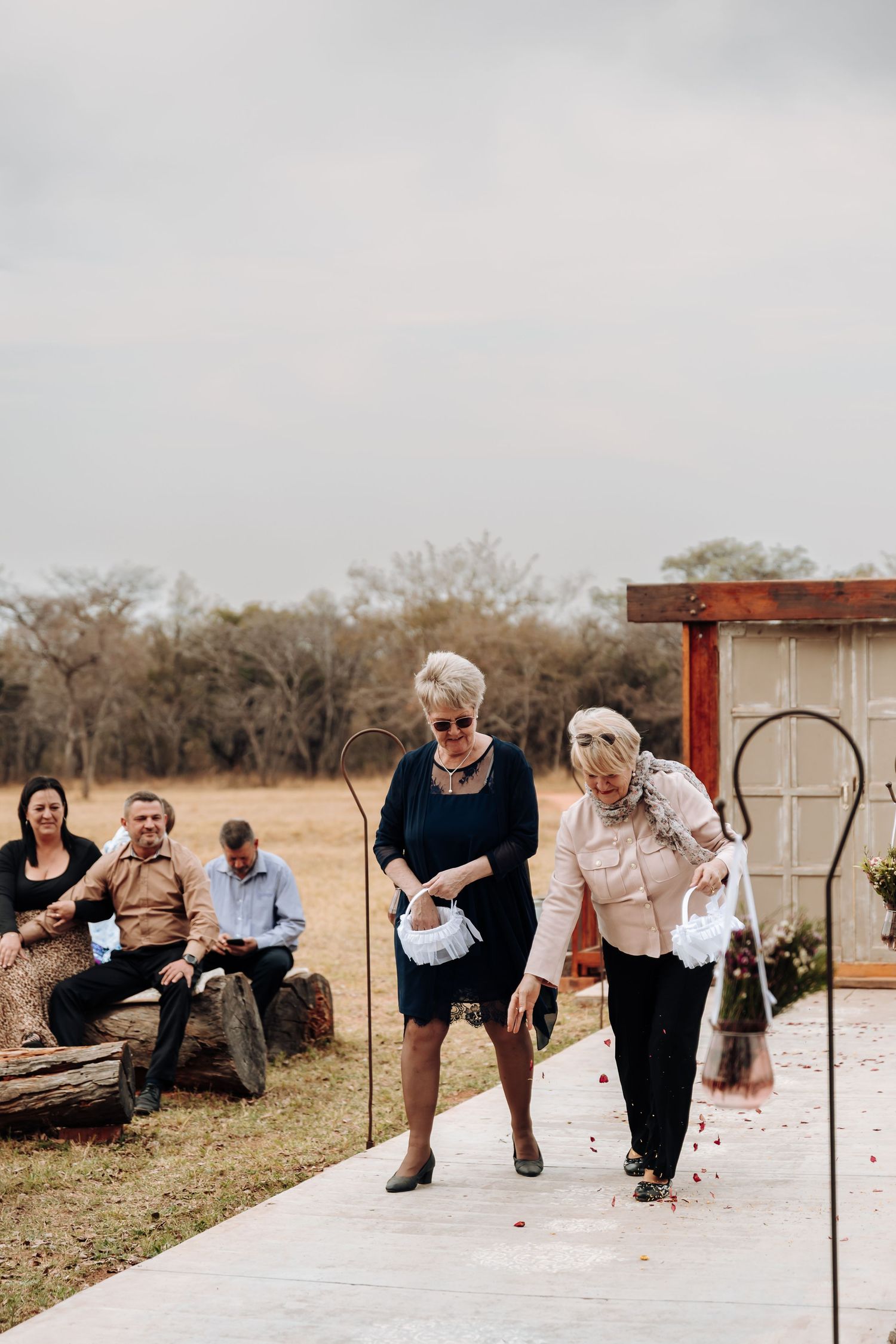 Two elderly ladies walk together down a concrete path while others sit on benches in the background.
