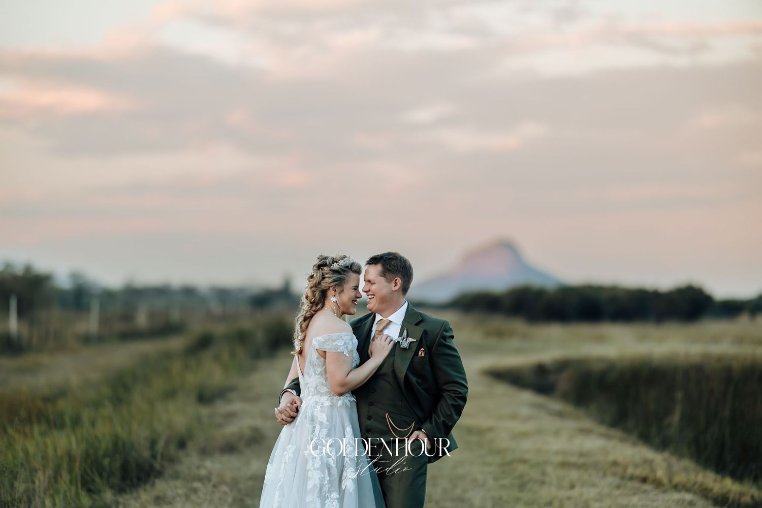 Bride and groom sharing an intimate moment in a golden field at sunset with a mountain backdrop.