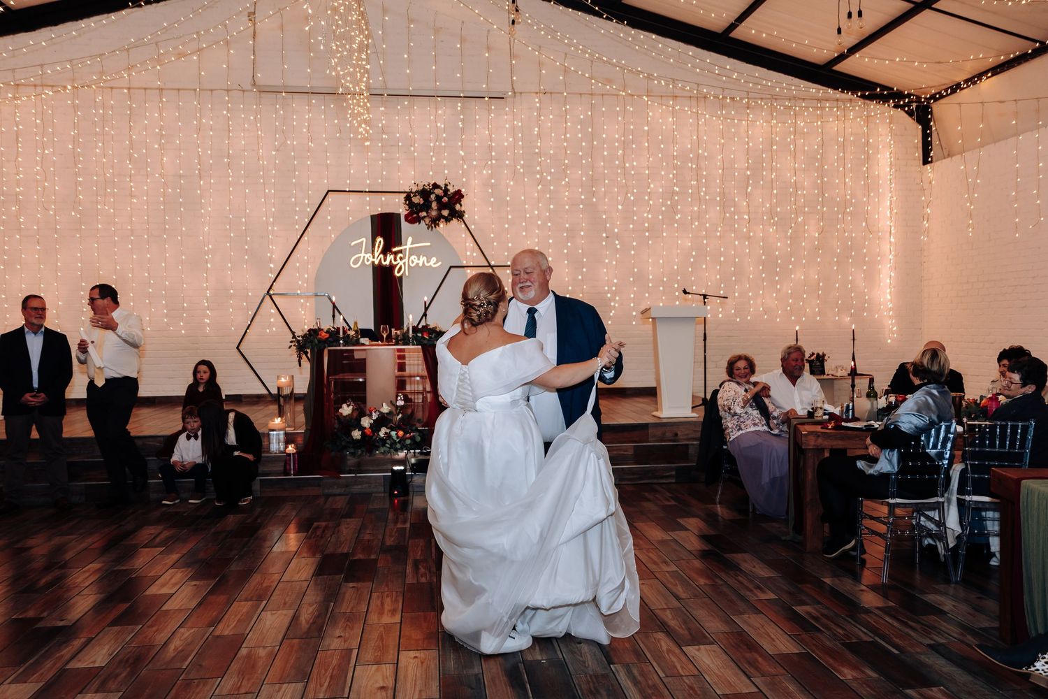Bride and groom share their first dance under fairy lights at a rustic wedding reception venue.