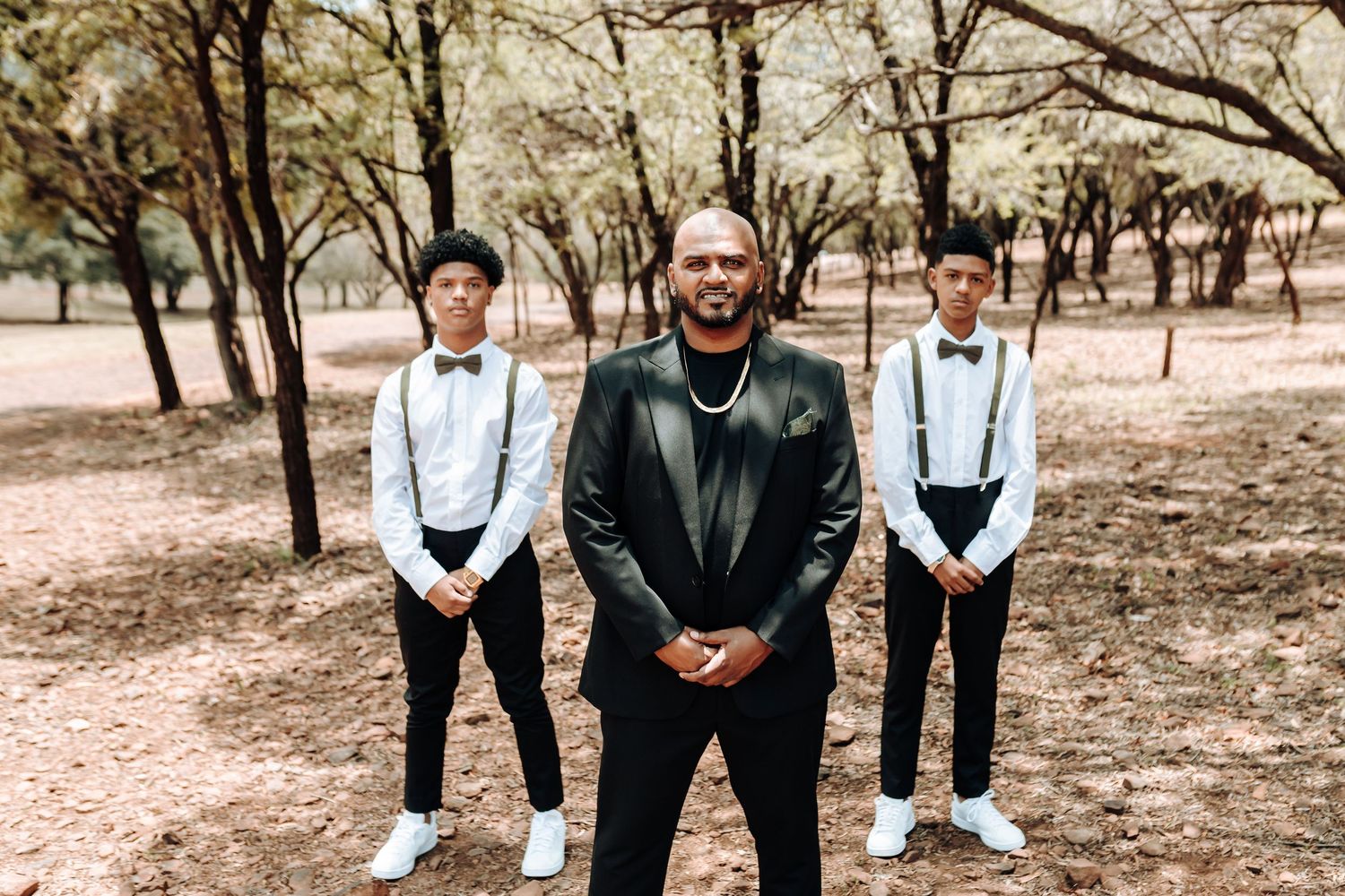 Three people in formal attire posing together in outdoor setting.