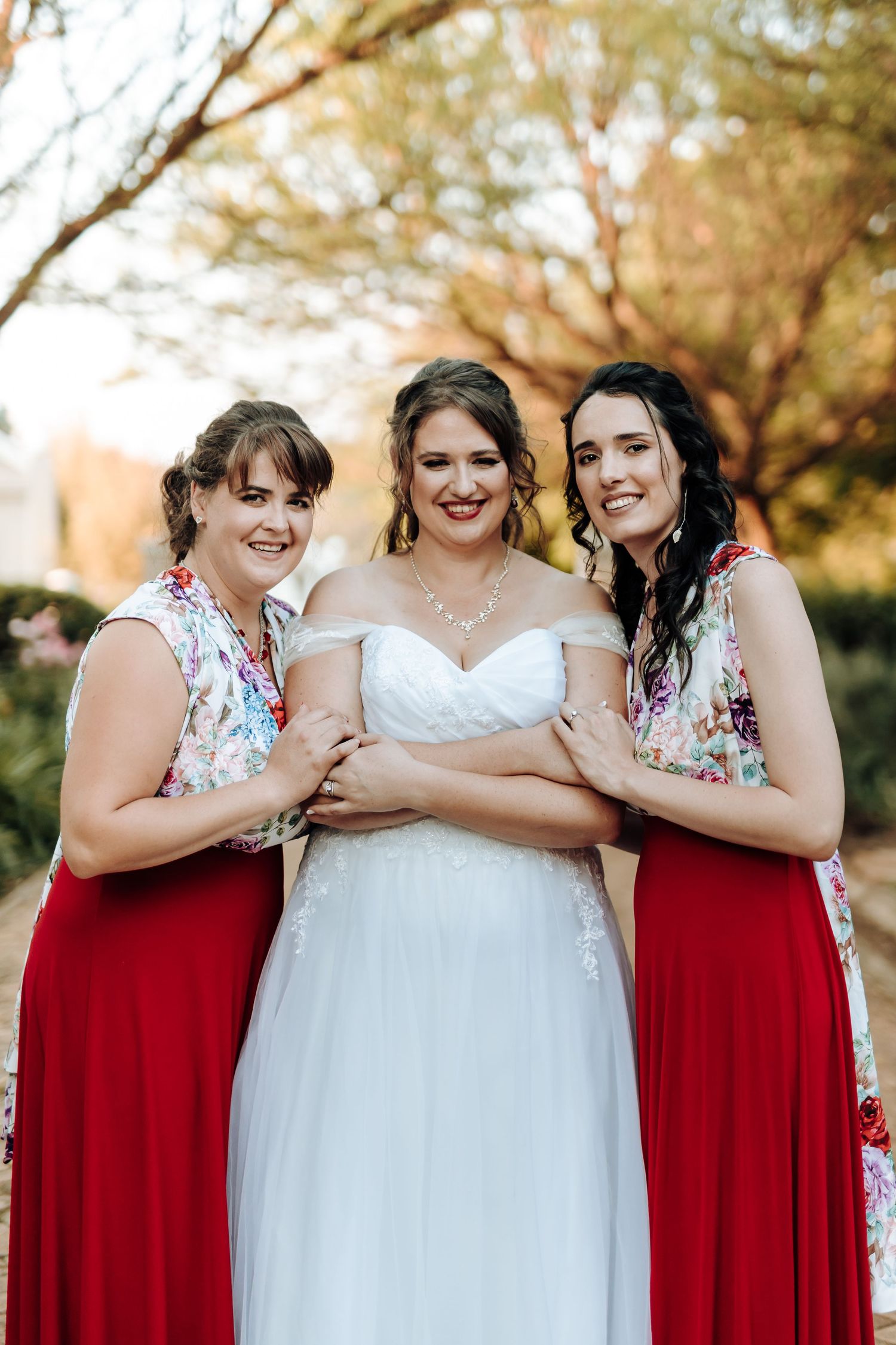 Bridal party in red and white floral dresses pose together outdoors.