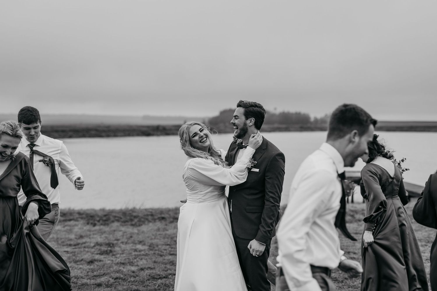 Black and white candid moment of wedding party celebrating outdoors by water.