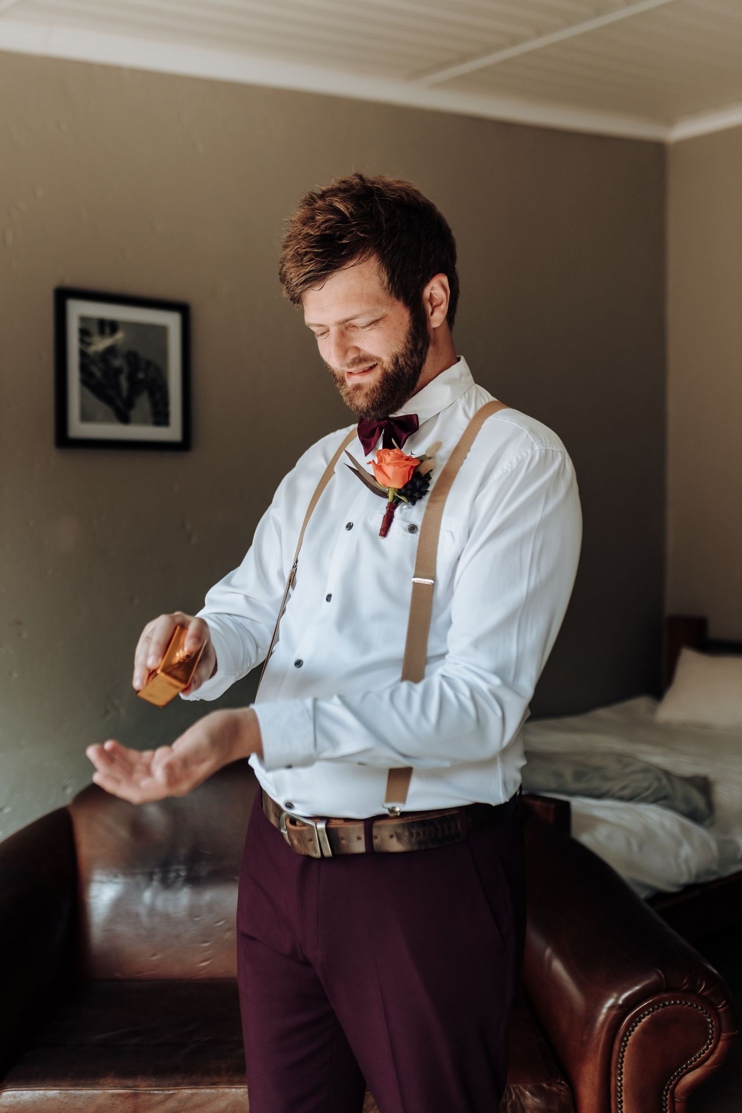 Wedding party member in white shirt and burgundy pants adjusts cufflinks while getting ready.