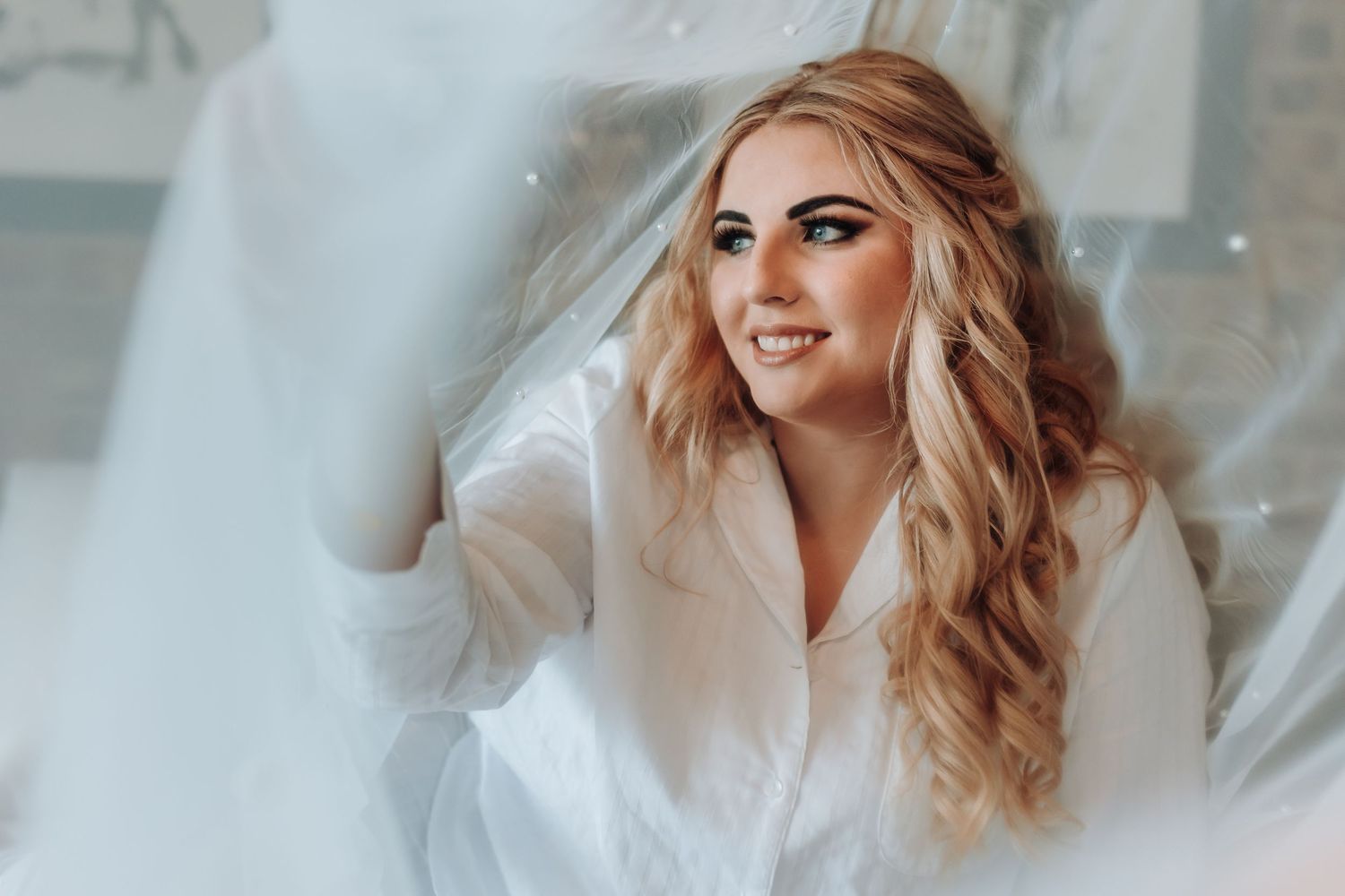 A close-up portrait showing flowing blonde curls and a white garment against a dreamy background.