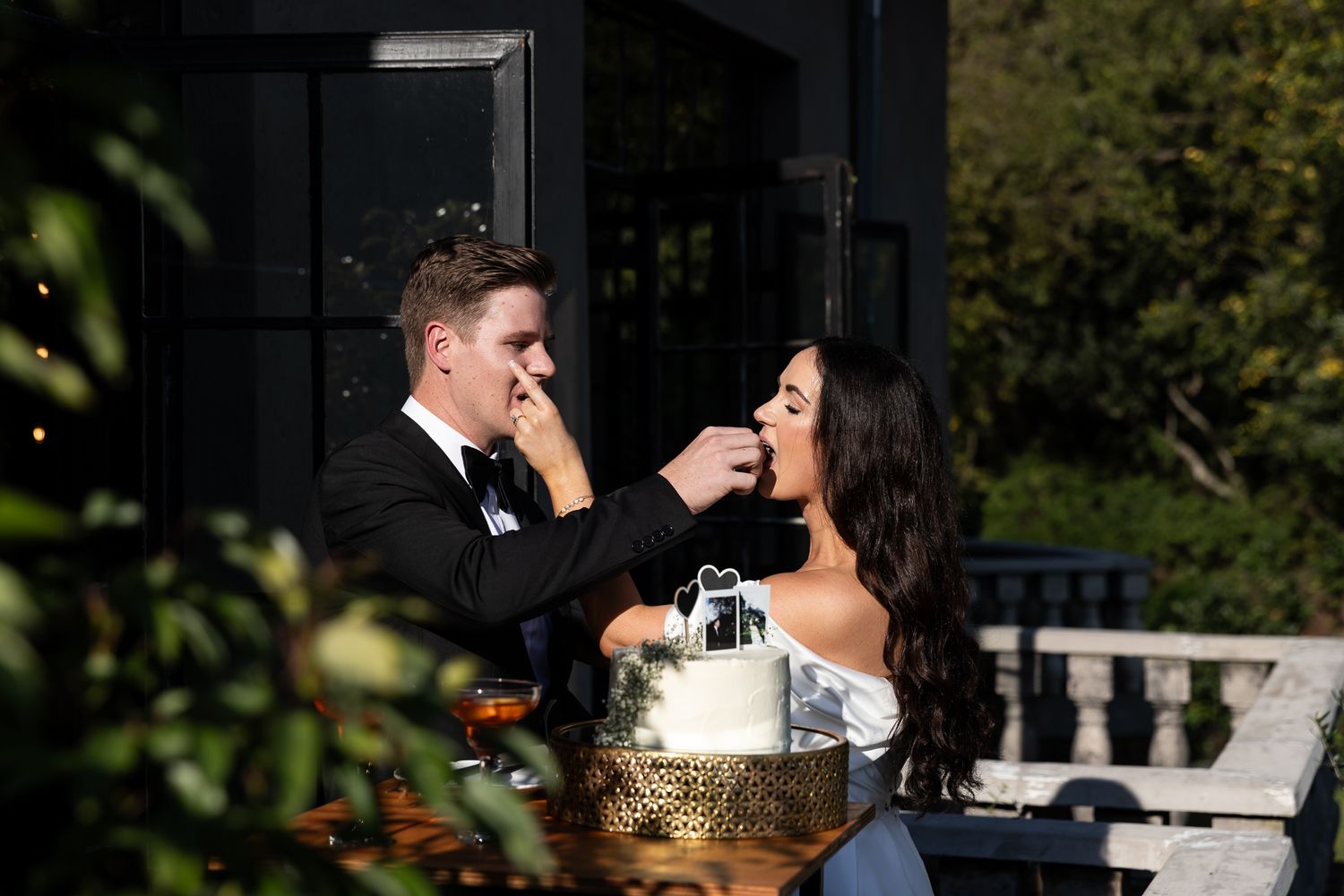 A couple playfully feeds each other wedding cake during their outdoor reception.