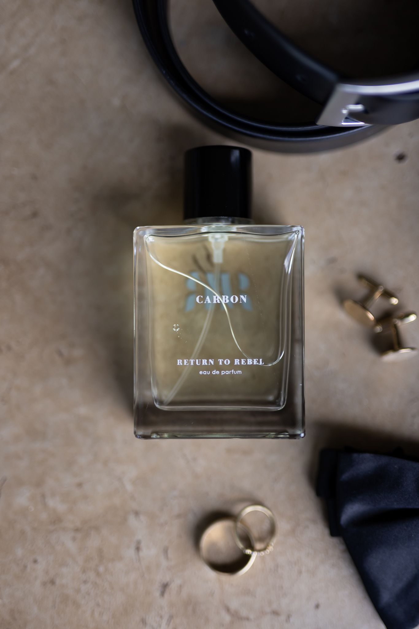 A bottle of Carbon perfume surrounded by jewelry and accessories on a concrete surface.