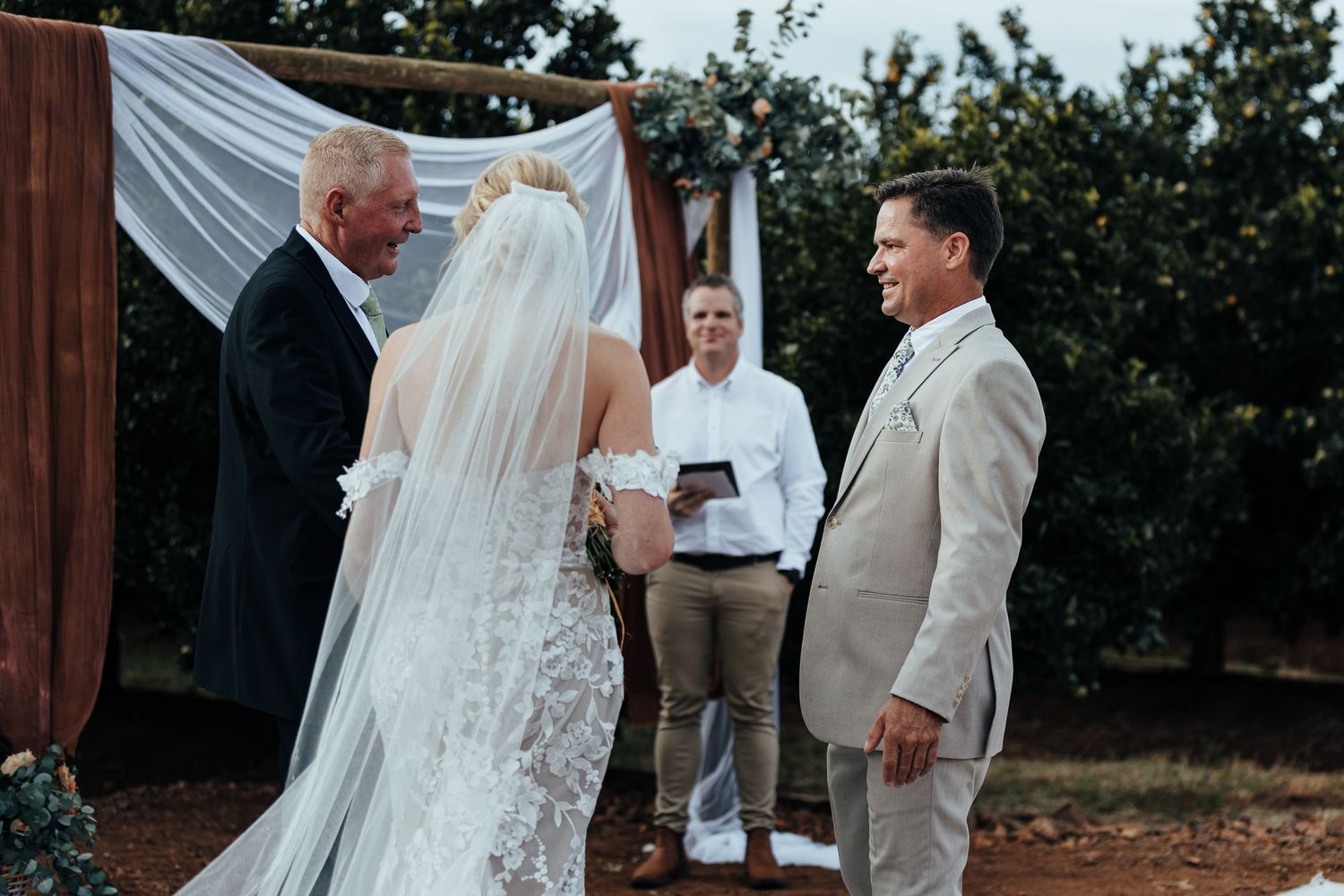 Outdoor wedding ceremony with white fabric backdrop and officiant leading the vows.