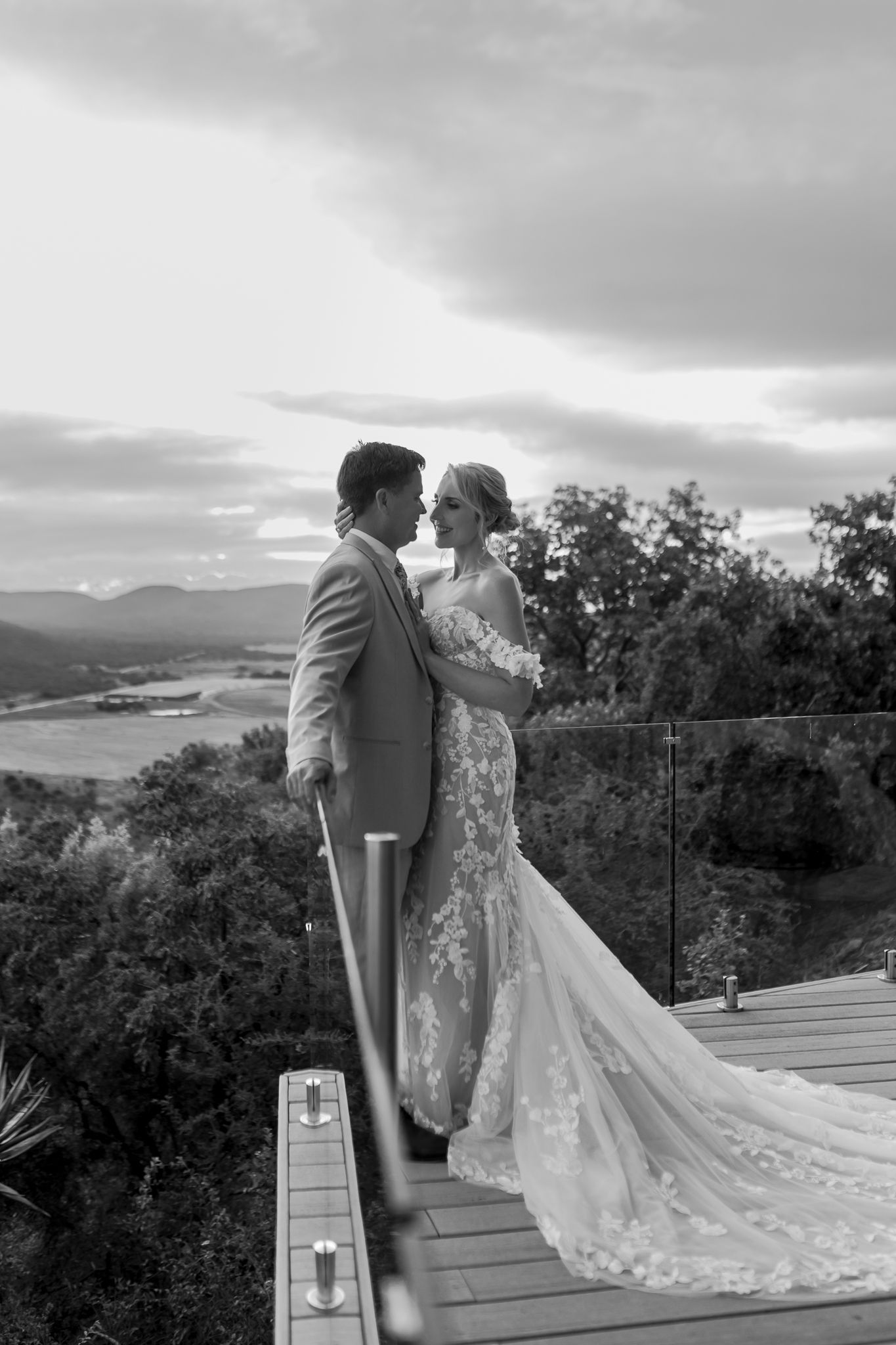 Black and white wedding portrait of a couple on a scenic overlook with mountains in the distance.