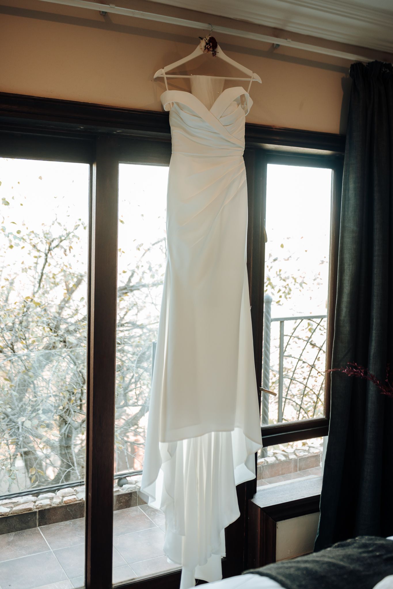 Elegant white wedding dress with sweetheart neckline hung against window with natural lighting.