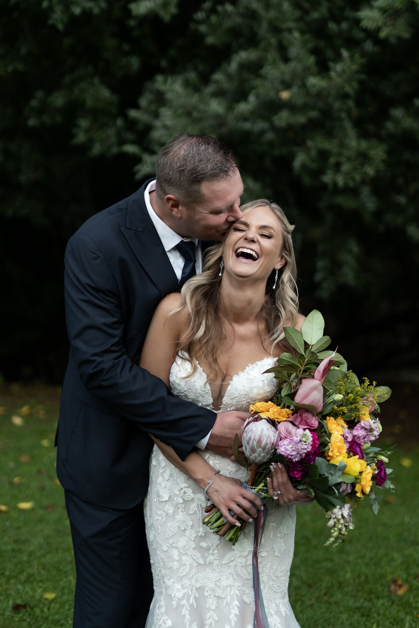 Candid moment of laughter between couple during wedding photoshoot with colorful bouquet.