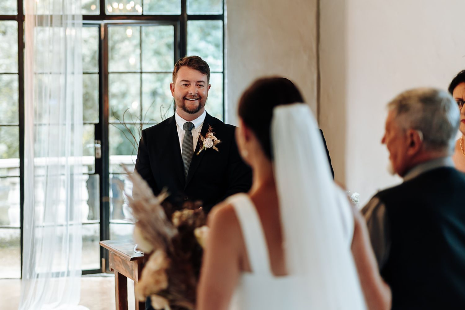 Wedding guests gather in a bright indoor venue with large windows during a joyful celebration ceremony.