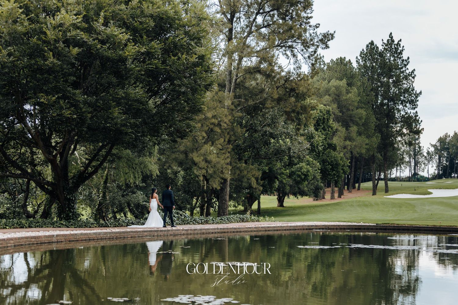 Scenic lakeside wedding venue with trees and water fountain in the background.