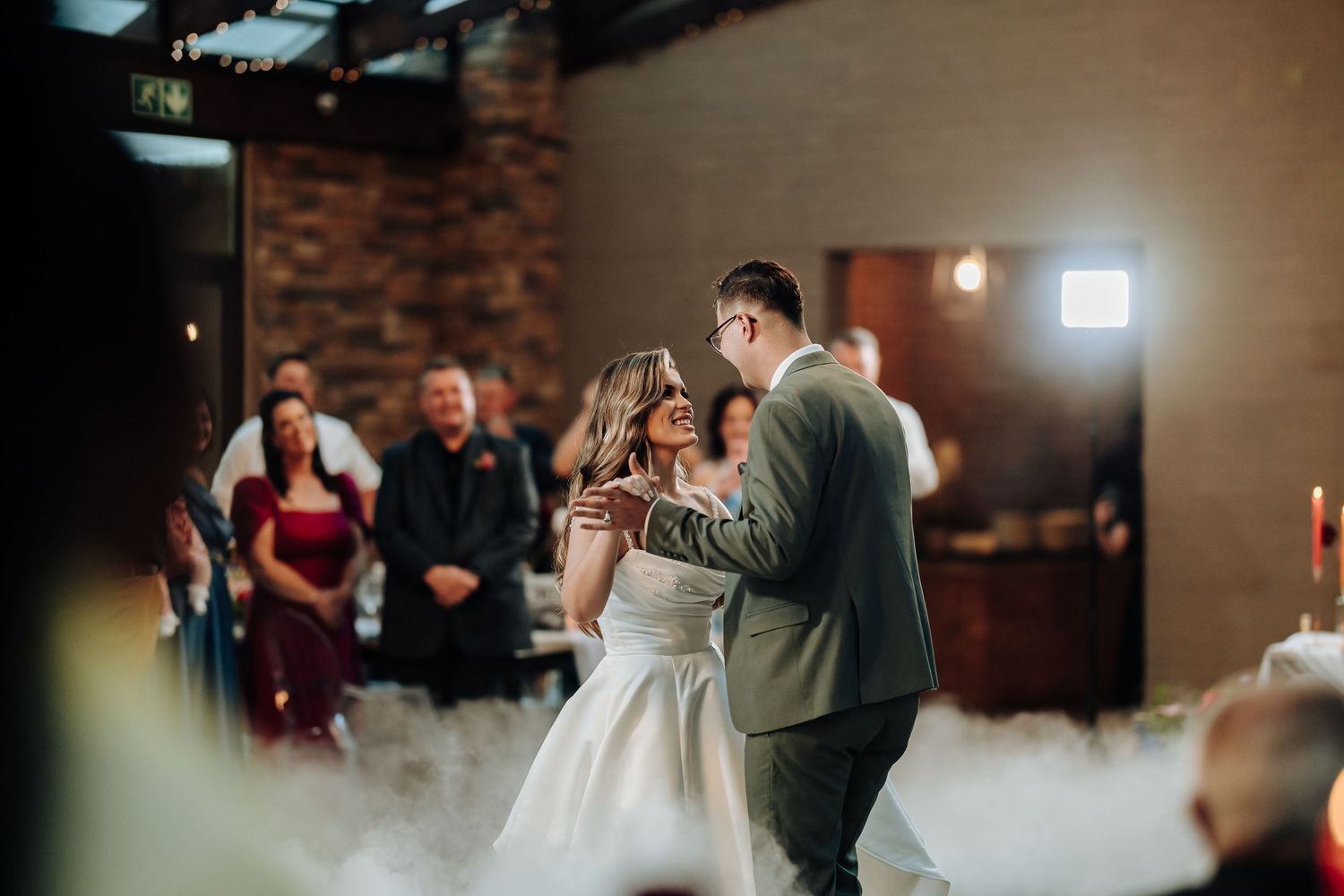 Wedding guests dancing together in a rustic venue with exposed brick walls and ambient lighting.